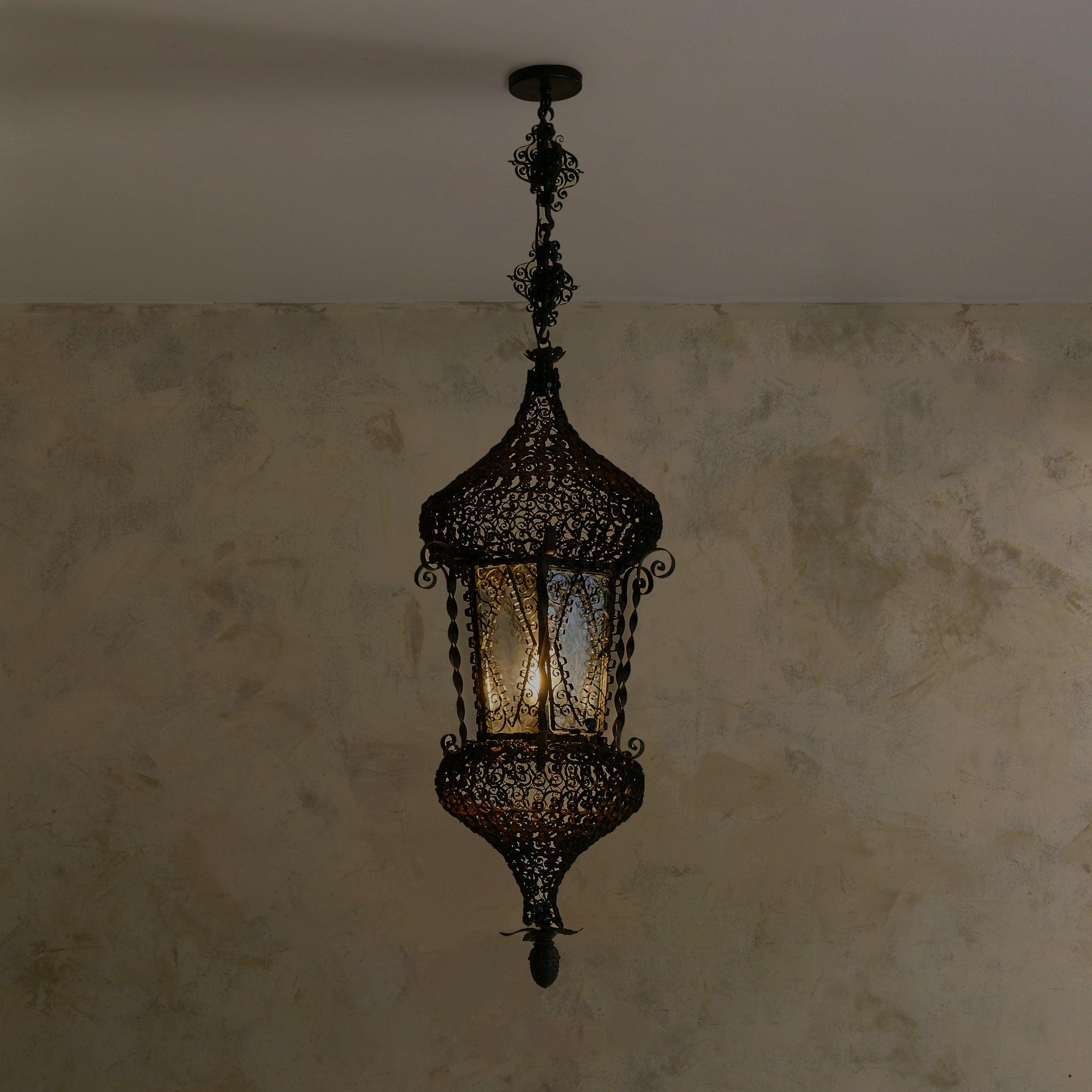A monumental Italian lantern pendant, handcrafted in Italy in the early 1900s. The dome-like form is wrapped in intricate wrought iron filigree—each scroll bent and fixed by hand into a lace-like mesh. Twisted uprights frame textured glass panes,