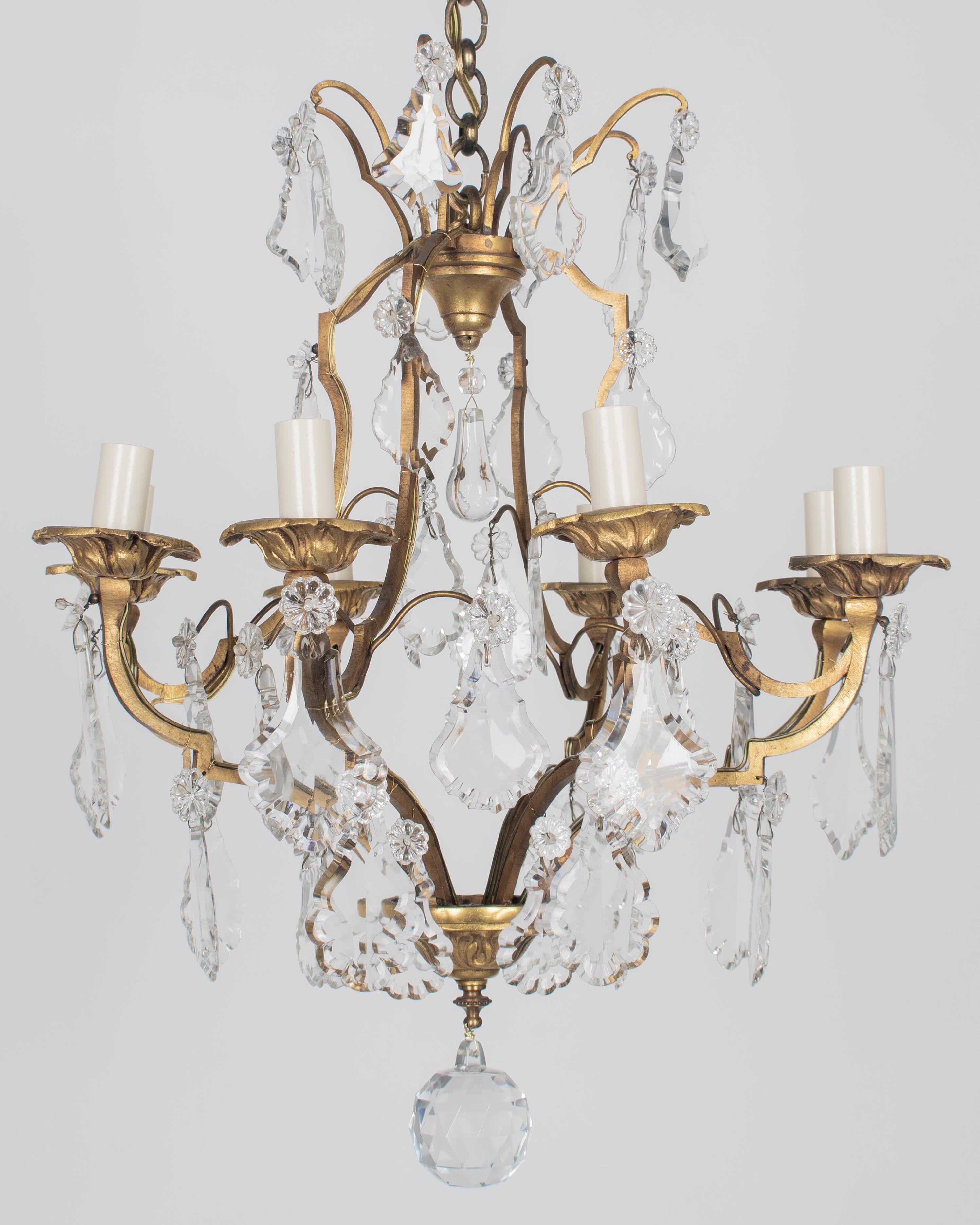 A French Louis XV style eight-light brass chandelier with an assortment of crystal prisms and pendalogues with rosettes. Solid brass frame with cast brass bobèches, chain and canopy. Rewired and in working condition. New sockets and candle covers.