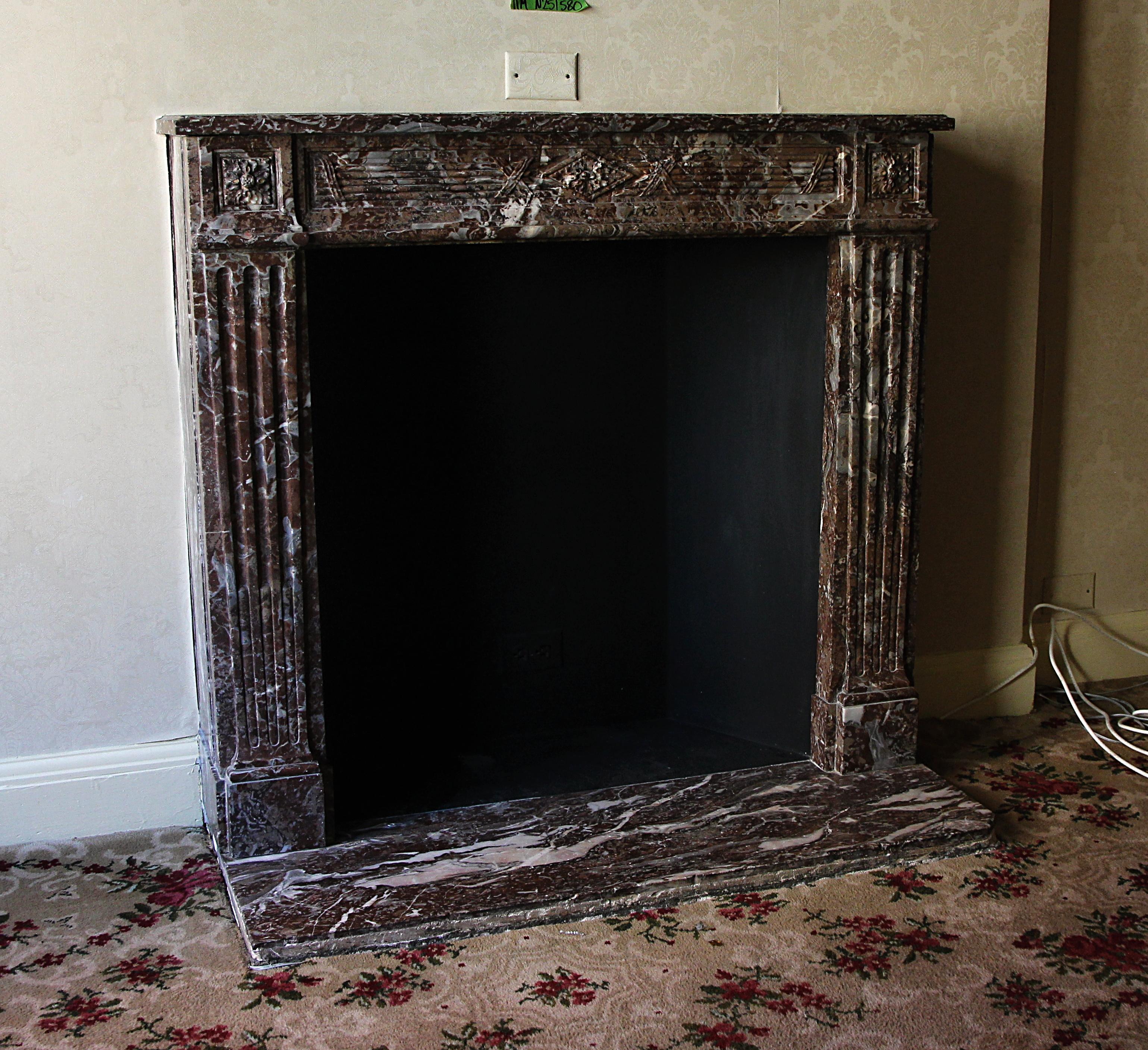 Hearth not included. Carved earth tone dark brown and grey marble Louis XVI French Regency mantel from the early 20th century. This petite mantel was one of a group of antique mantels imported from France and installed in the Waldorf Astoria hotel