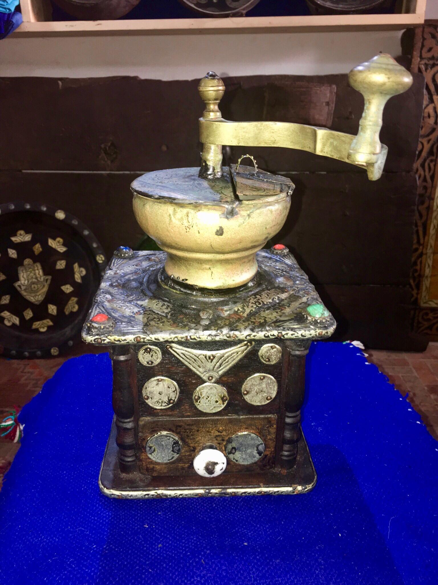 This antique hand-crank grinder is made of ebony wood, with hand-engraved silver melange adornment, hand carved camel bone embellishments, and numerous antique coins. Entirely handmade, this grinder was used by southern Morocco nomads while