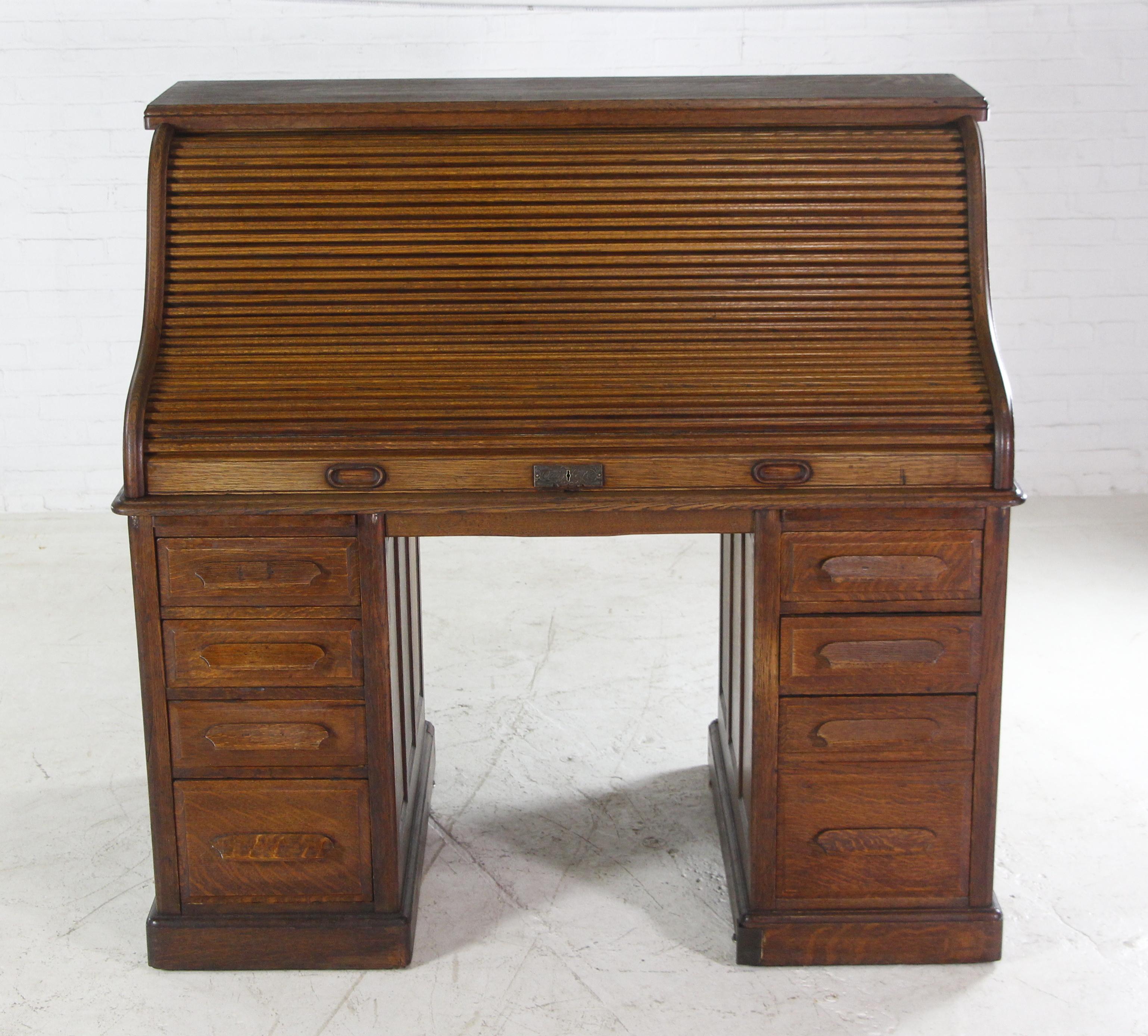 This antique oak roll top desk has paneled sides and back with a tambour slatted front. It consists of seven drawers underneath a spacious top with several pigeonhole and letter compartments. Made by Quigley Co. This can be seen at our 2420 Broadway