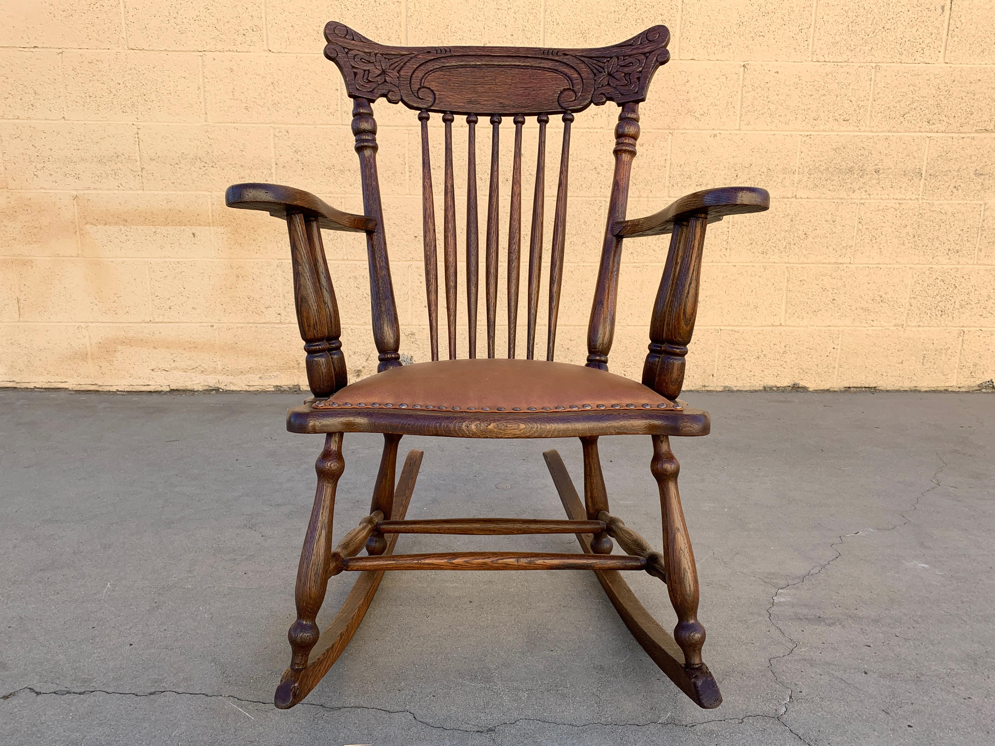 Very old press back oak rocking chair, circa early 1900s. Features reconditioned oak frame and new leather seat with brass upholstery tacks. Good antique condition with minimal signs of wear.

Dimensions: 26” W x 34” D x 35” H
Seat height 16” H.