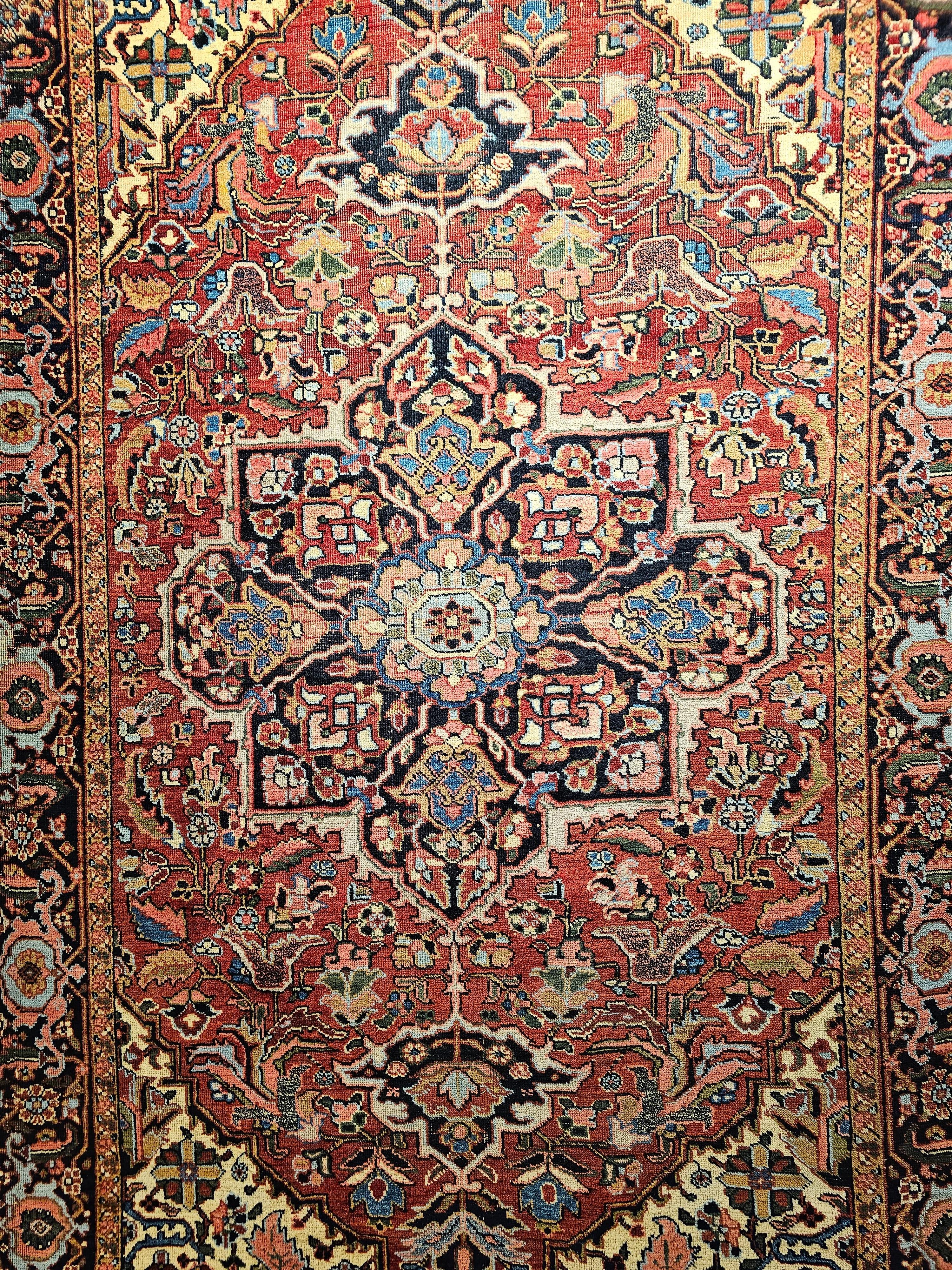 A vintage room size Persian Heriz from the 1st quarter of the 1900s. It has a burgundy color field and a navy blue border. The rug has a large format design and beautiful combination of colors including yellow, baby blue, pink, green and many others