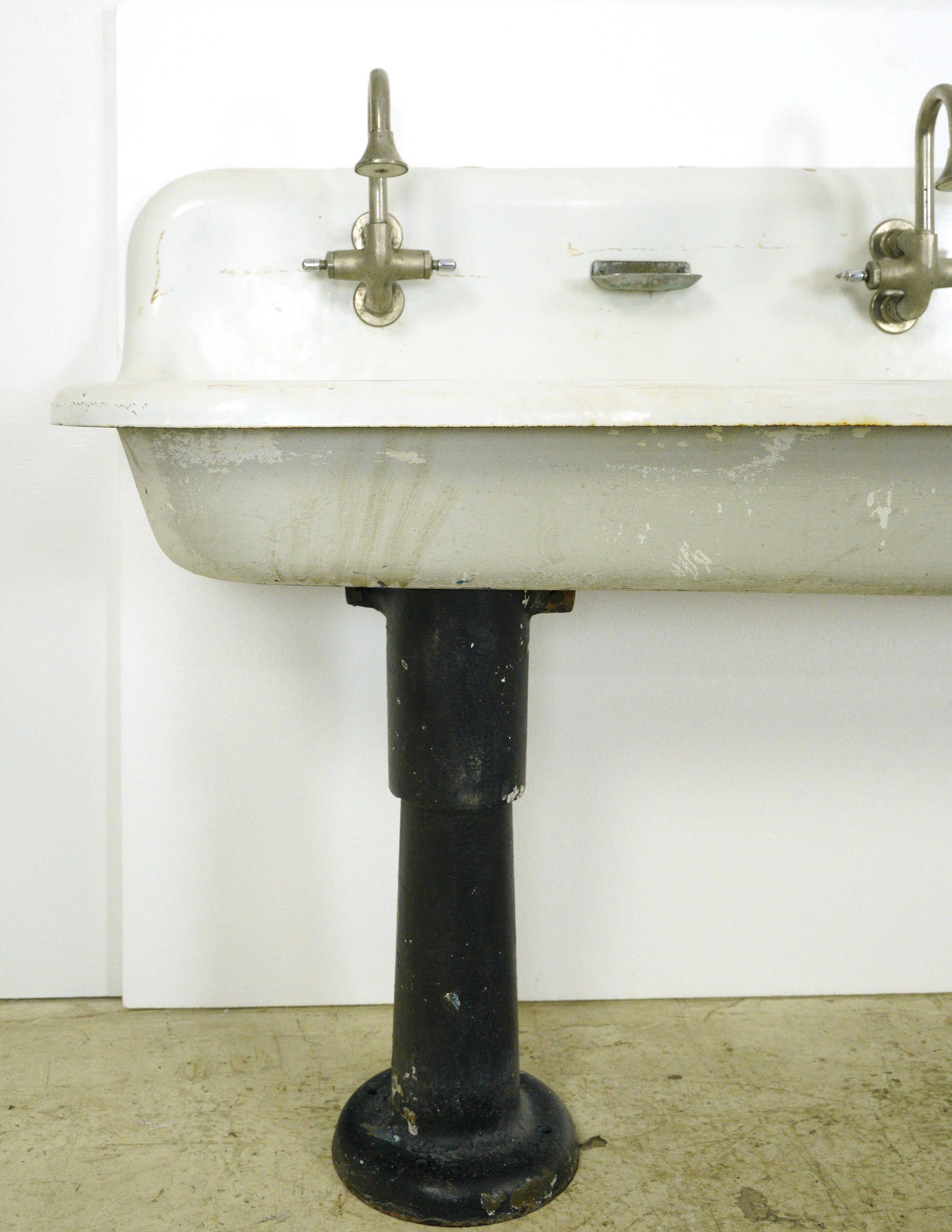 White porcelain over cast iron trough gang sink with four faucets. The Kohler stainless steel soap dishes and faucets are included. Good condition with surface wear from prior use. One available. Please note, this item is located in our Scranton, PA