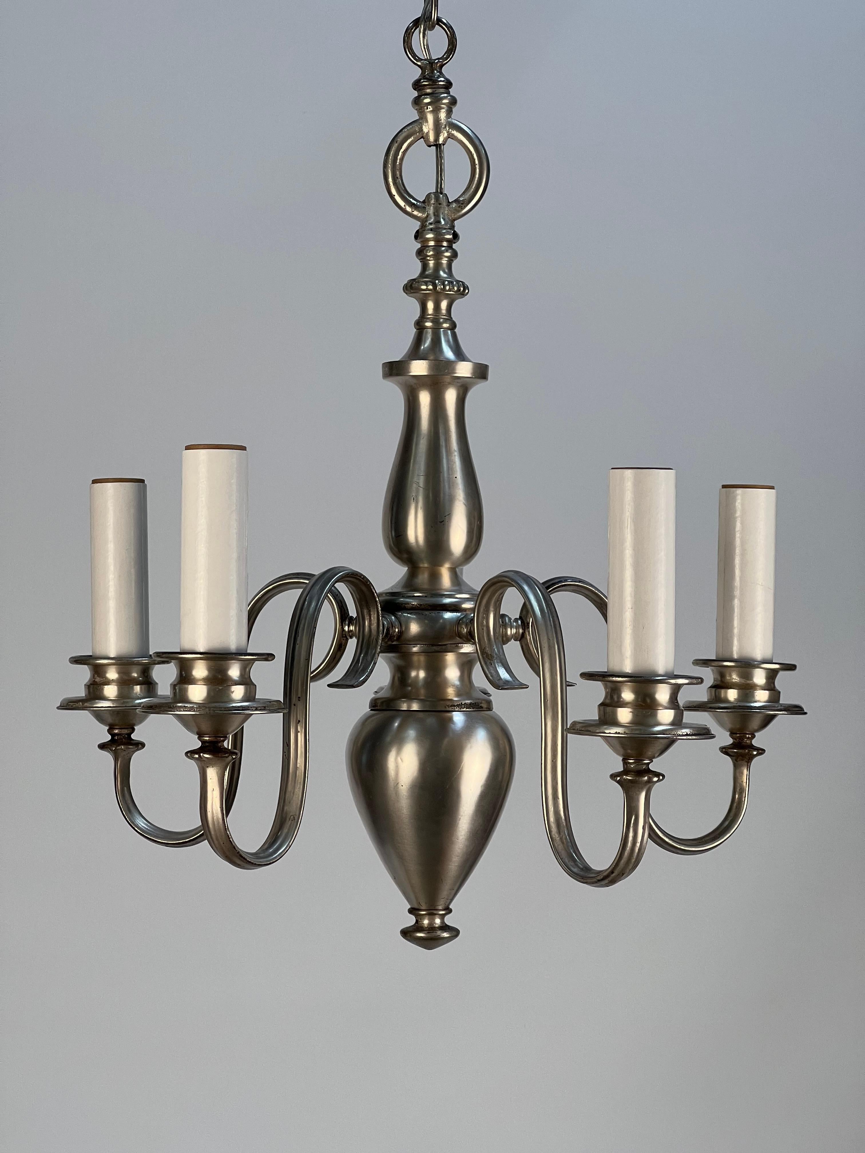 A high-end early 1920's silvered chandelier featuring five scrolled arms attached to a central arabesque body. The shapes and curves of the chandelier suggest quiet elegance and opulence. The patina of the silvered brass has aged with grace only