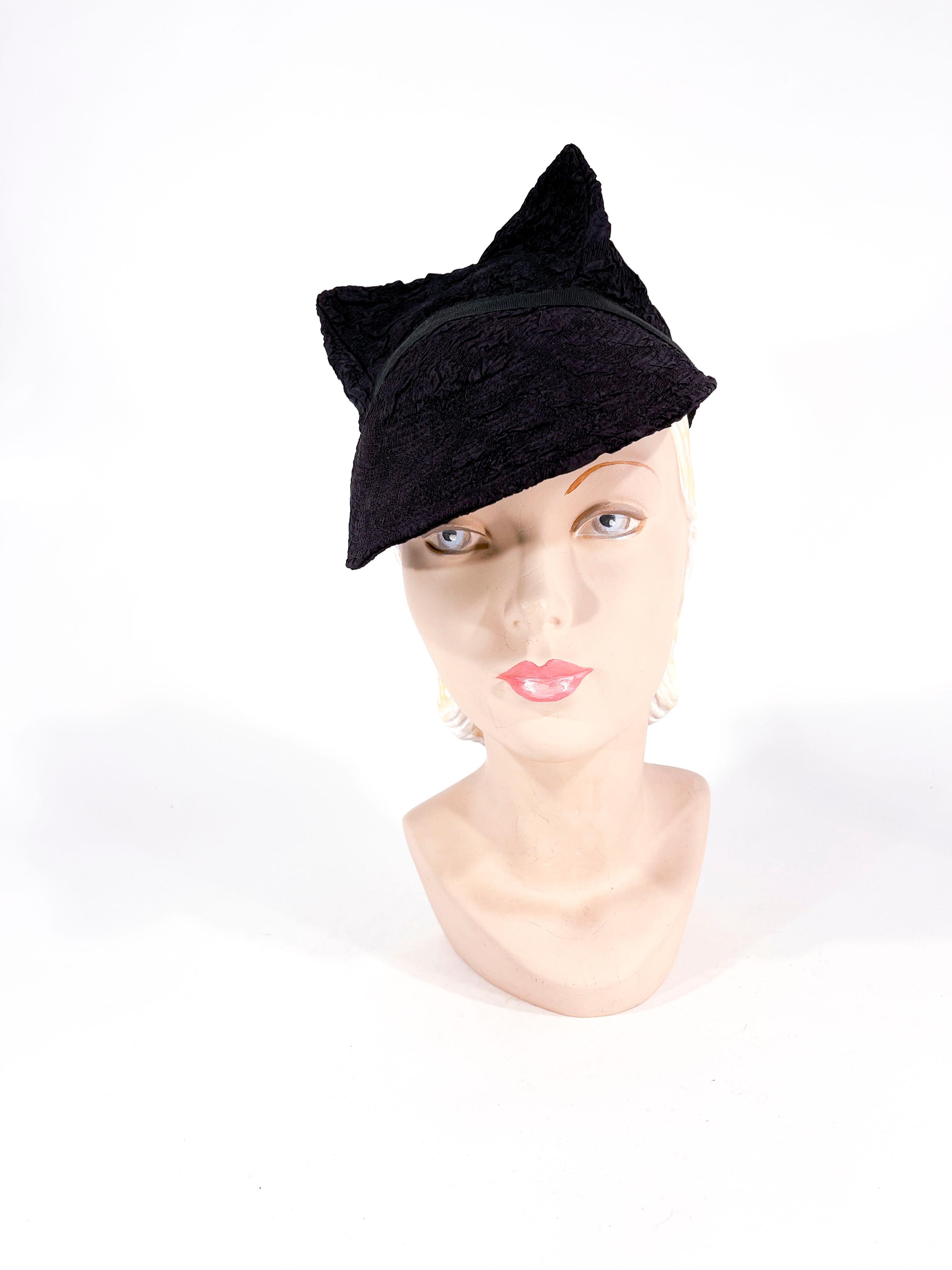 Eleganter Art-Déco-Damenhut aus den frühen 1930er Jahren aus schwarzem strukturiertem Viskosegewebe. Die Silhouette des Hutes besteht aus einer vergrößerten Vorderkrempe, einem Ripsband in der Mitte und zwei geformten Doppelspitzen. Das Innere des