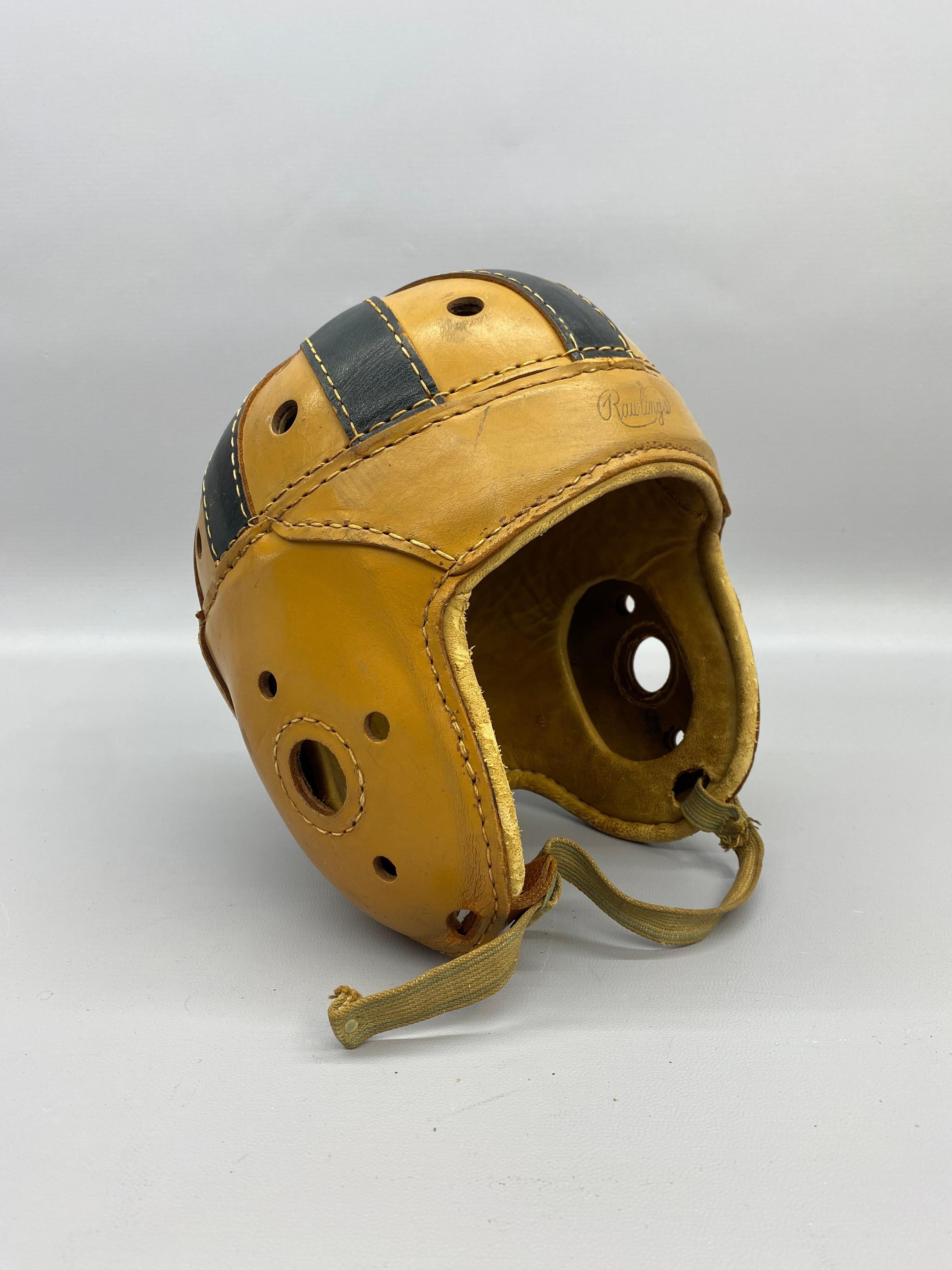 Ein Rawlings-Jugendfußballhelm aus Leder aus den frühen 1950er Jahren. Vorgesichtsmaske. Der Helm ist eine Jugendgröße 7. Zweifarbiges Leder mit dunklen genähten Lederriemen auf der Oberseite des Helms mit Lüftungslöchern. Geprägter
