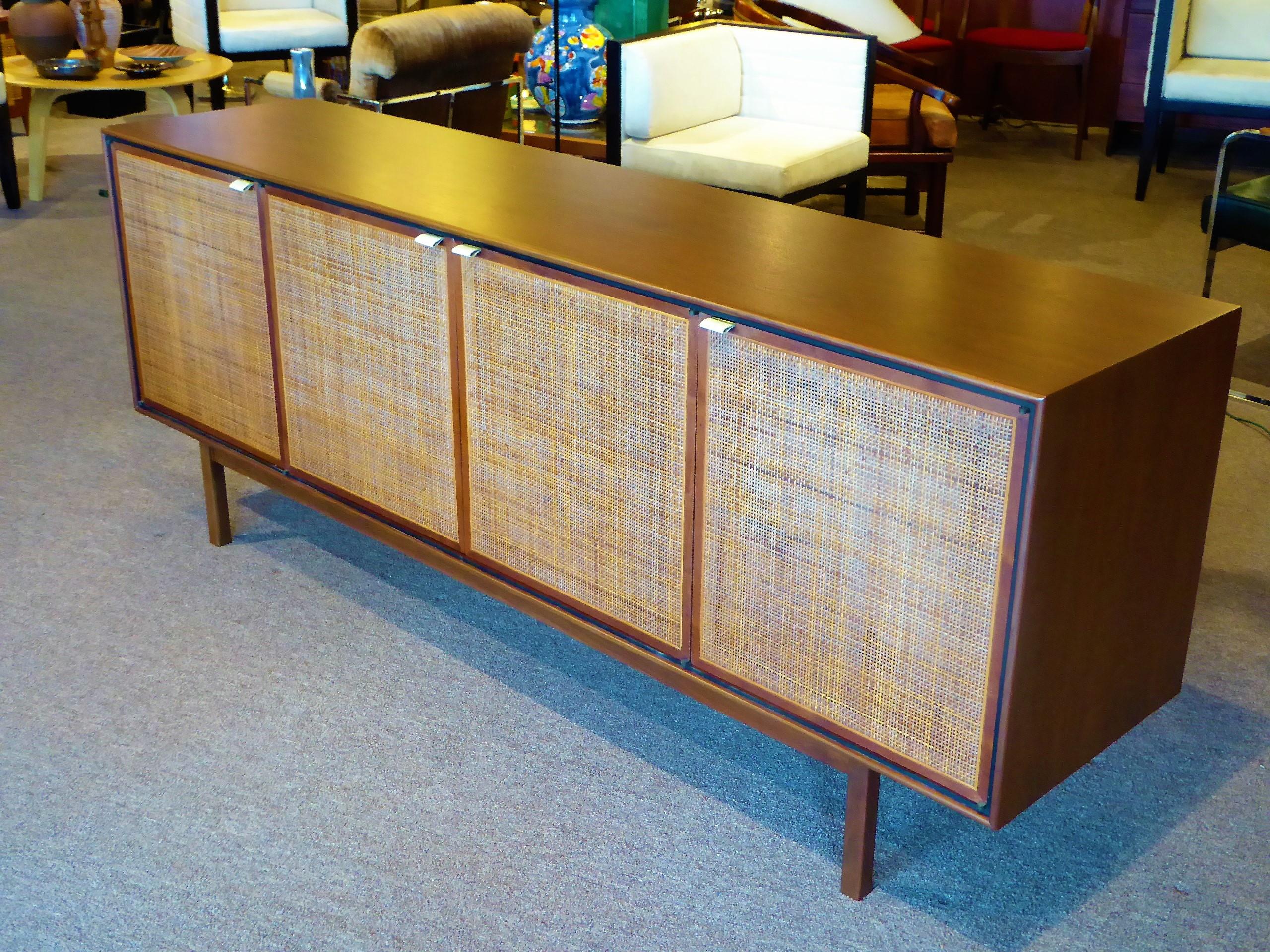 A beautifully designed and constructed credenza by Founders Furniture, probably a Jack Cartwright design, it features a figured walnut case body with cane front doors and leather tab pulls supported by a rectilinear base. Doors conceal two