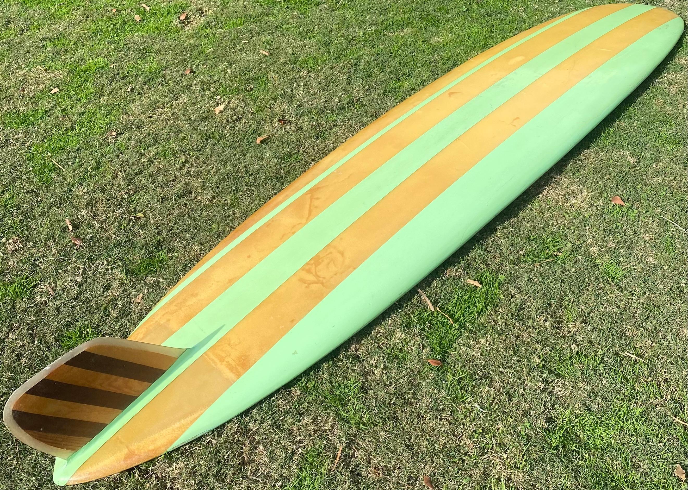 Early-1960s Velzy Surfboards pintail longboard. Features beautiful seafoam green stripes with balsa wood stringer and 7 piece wooden fin. “The Surfboard of Champions” silver-foil logo. A remarkable original example of an early 1960s longboard shaped