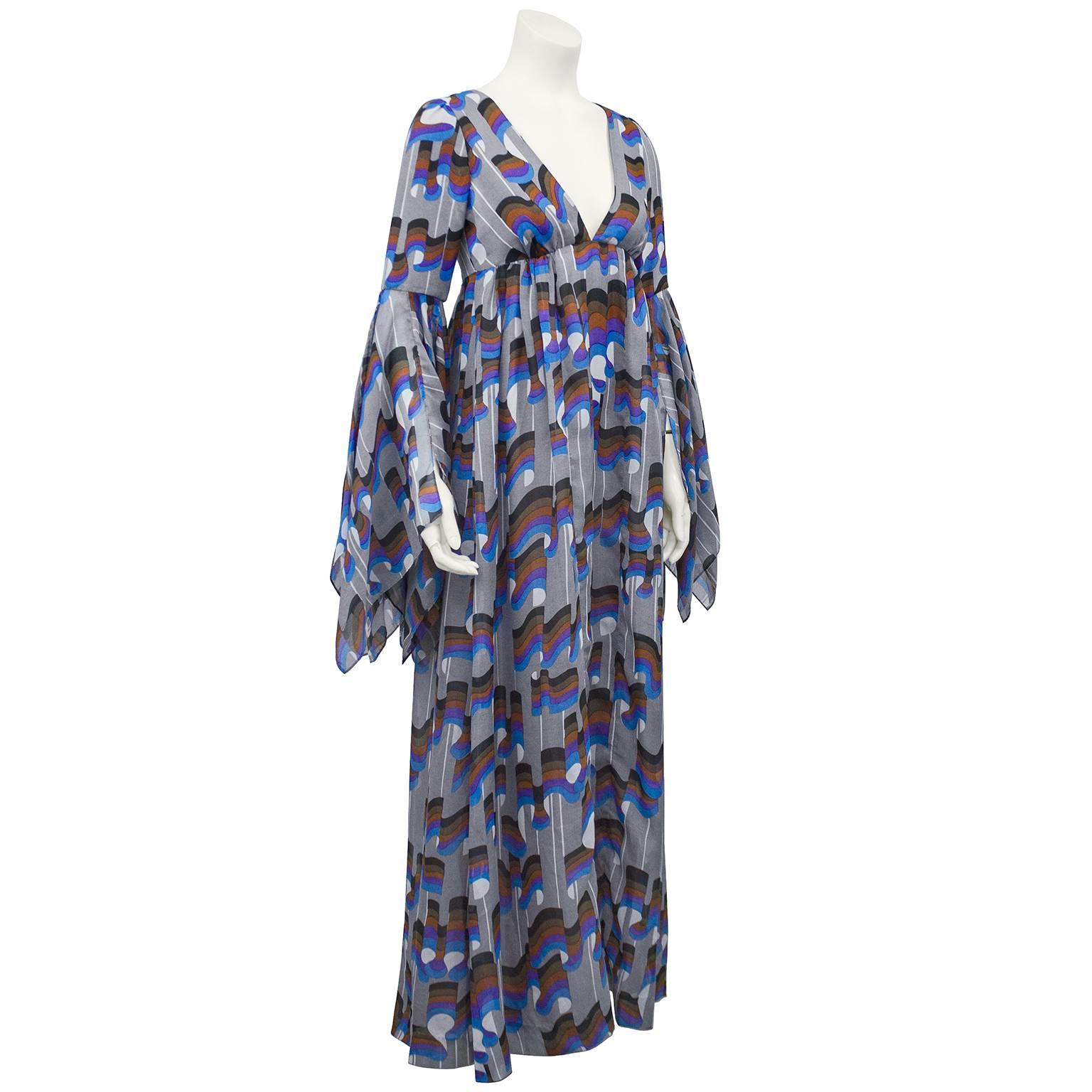 Stunning early 1970s Jean Varon boho style gown. Grey cotton with a black, brown, purple, blue and white mod print throughout. Deep v neck, empire waist and long, full skirt. Sleeves cinch just above elbow and flare out with a hanky hem. Excellent