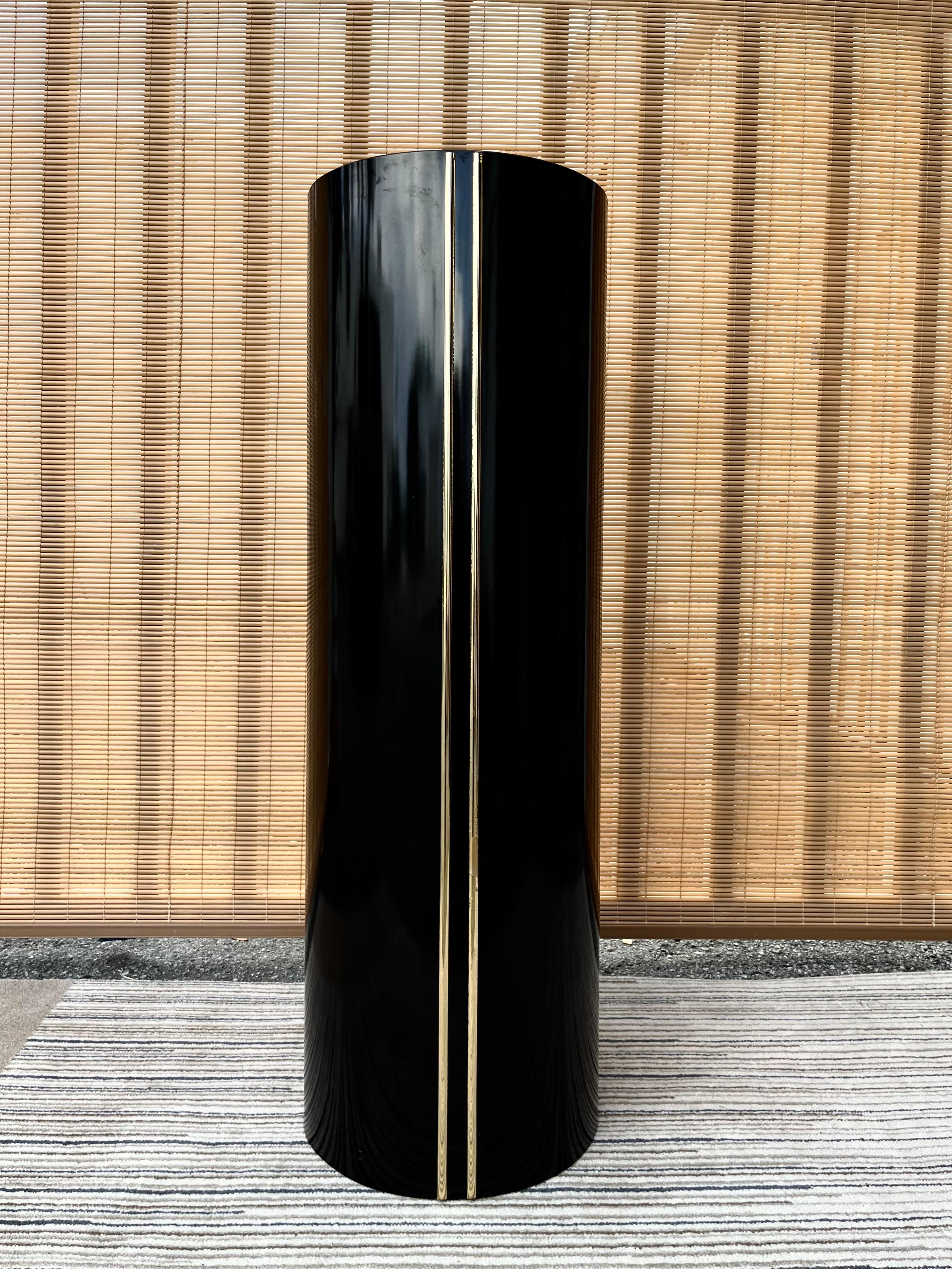 Vintage postmodern black and gold formica display pedestal/ column. Circa Early 1980s.
Feature a minimalist cylindrical shape laminated with black Formica with two parallel brass pleated trims at the front. 
In excellent original condition with