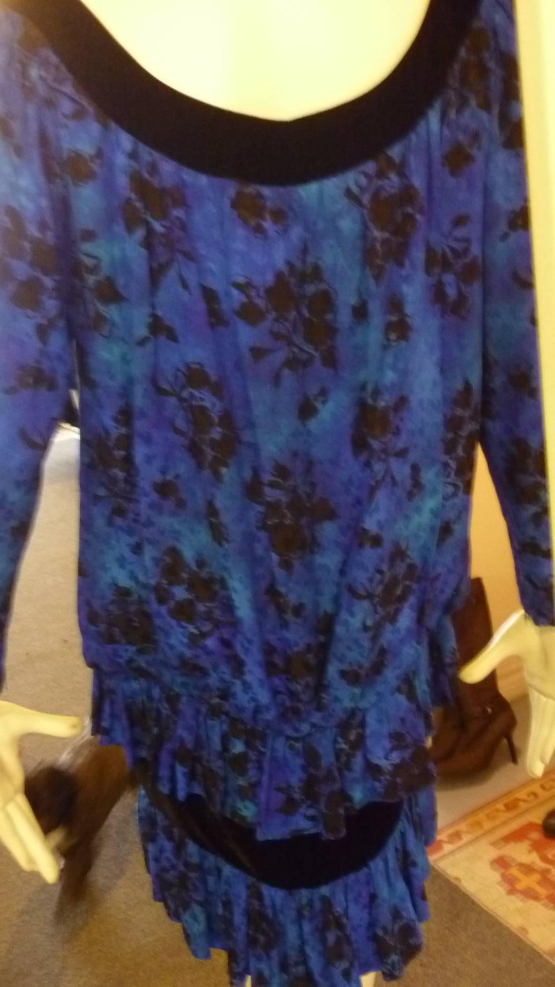 Typical of Yves Saint Laurent's 1980s style, this silk dress is in a lovely iridescent blue with a black floral print. There is a black velvet trim on the collar as well as a velvet panel on the skirt. The dress also features a dropped waist look