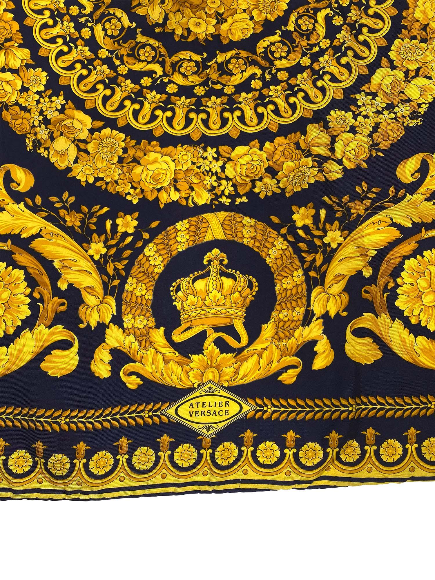 Presenting a beautiful baroque Atelier Versace square silk scarf, designed by Gianni Versace. This scarf features a classically gold Versace floral baroque pattern atop a navy background with crowns and an Atelier Versace logo.