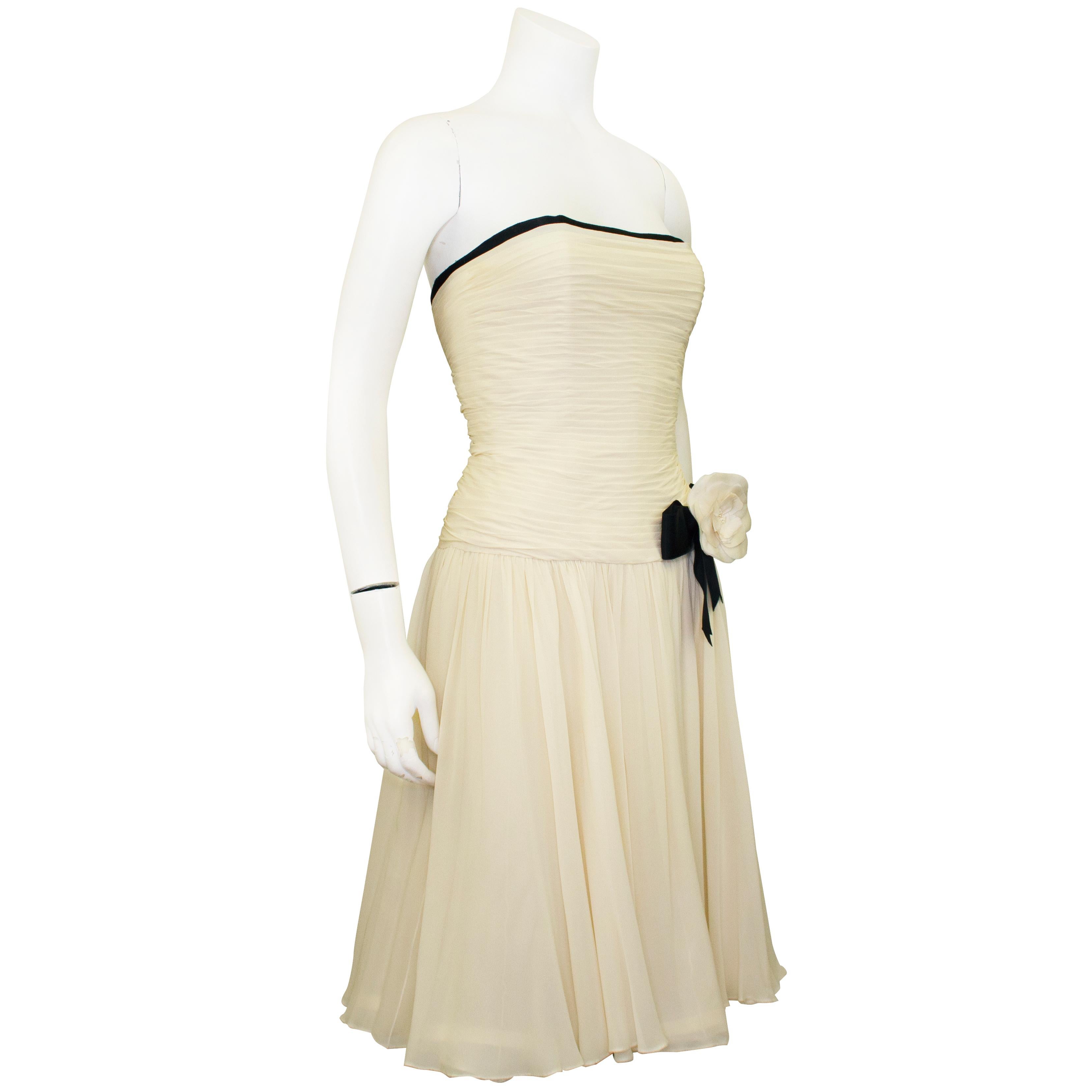 Beautiful Chanel strapless cream chiffon cocktail dress from the early 1990s. The bodice is a corset with interior boning and is textured with horizontal pleated and ruching. The black silk trim contrasts the cream chiffon perfectly. Flowing a line