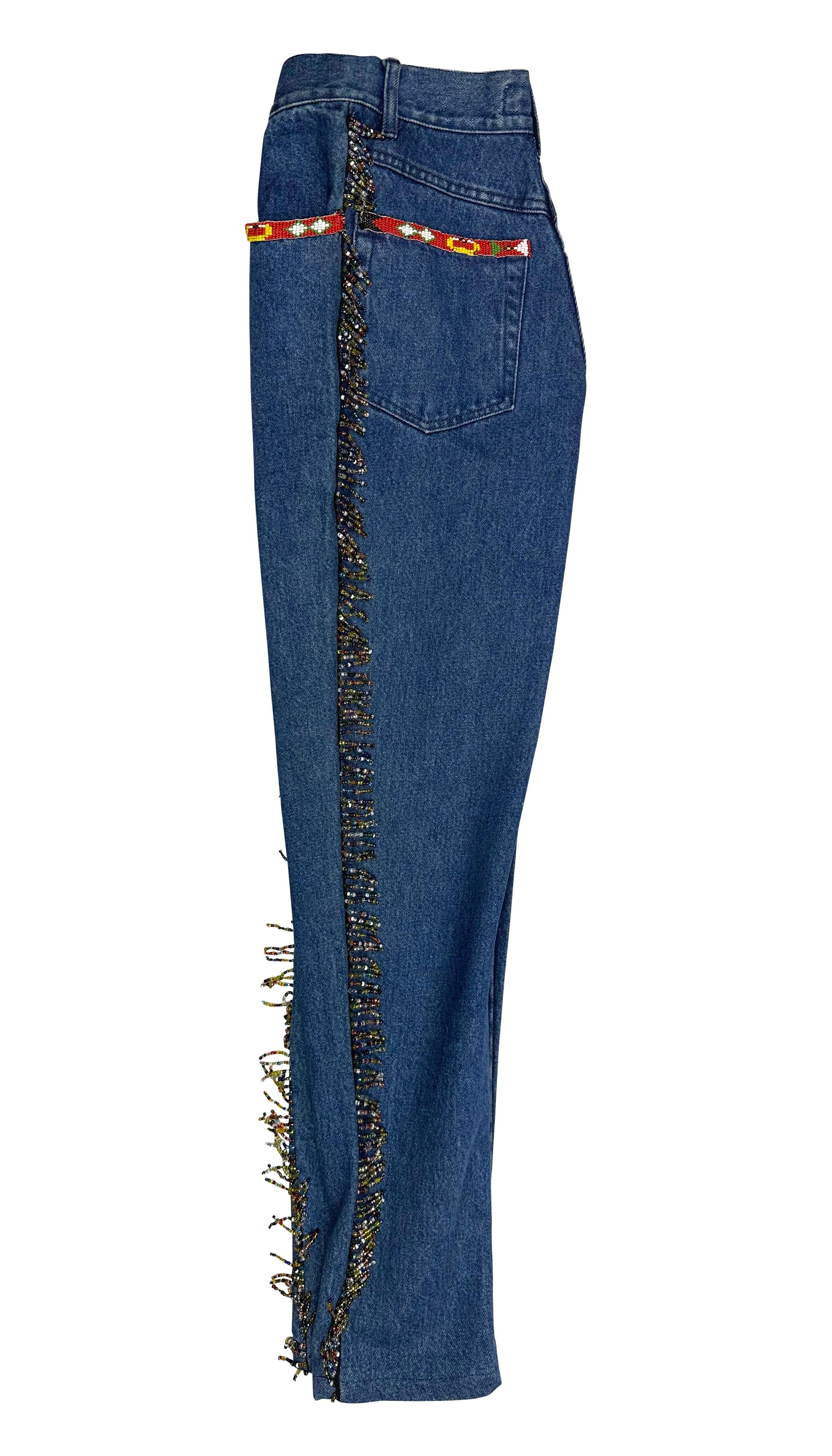 These early 1990s Dolce & Gabbana blue denim jeans feature a bold Western-inspired design, complete with intricate beaded fringe running down the sides. Colorful bead detailing around the front pockets adds a vibrant touch to the classic denim