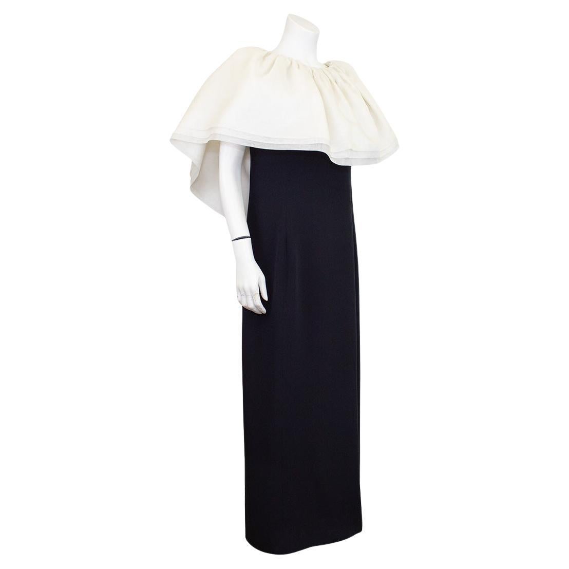 Stunning Stanley Platos black column gown with dramatic white organza ruffle neckline. The white ruffle falls from the top of the shoulders to the middle of the upper arm and is finished with a black bow on the back. In excellent condition, fits