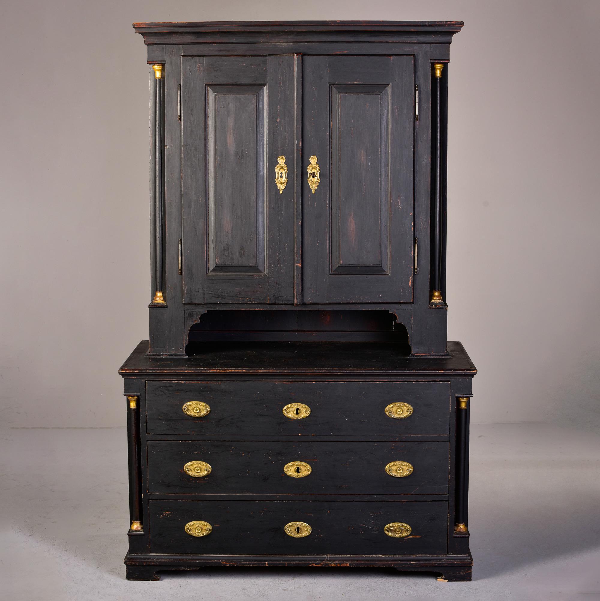 Circa 1810 Austrian linen cupboard has a black painted finish and brass hardware. Top section has two internal shelves and two small functional drawers with painted red interior. Lower section has three drawers, brass pulls. Top and base separate