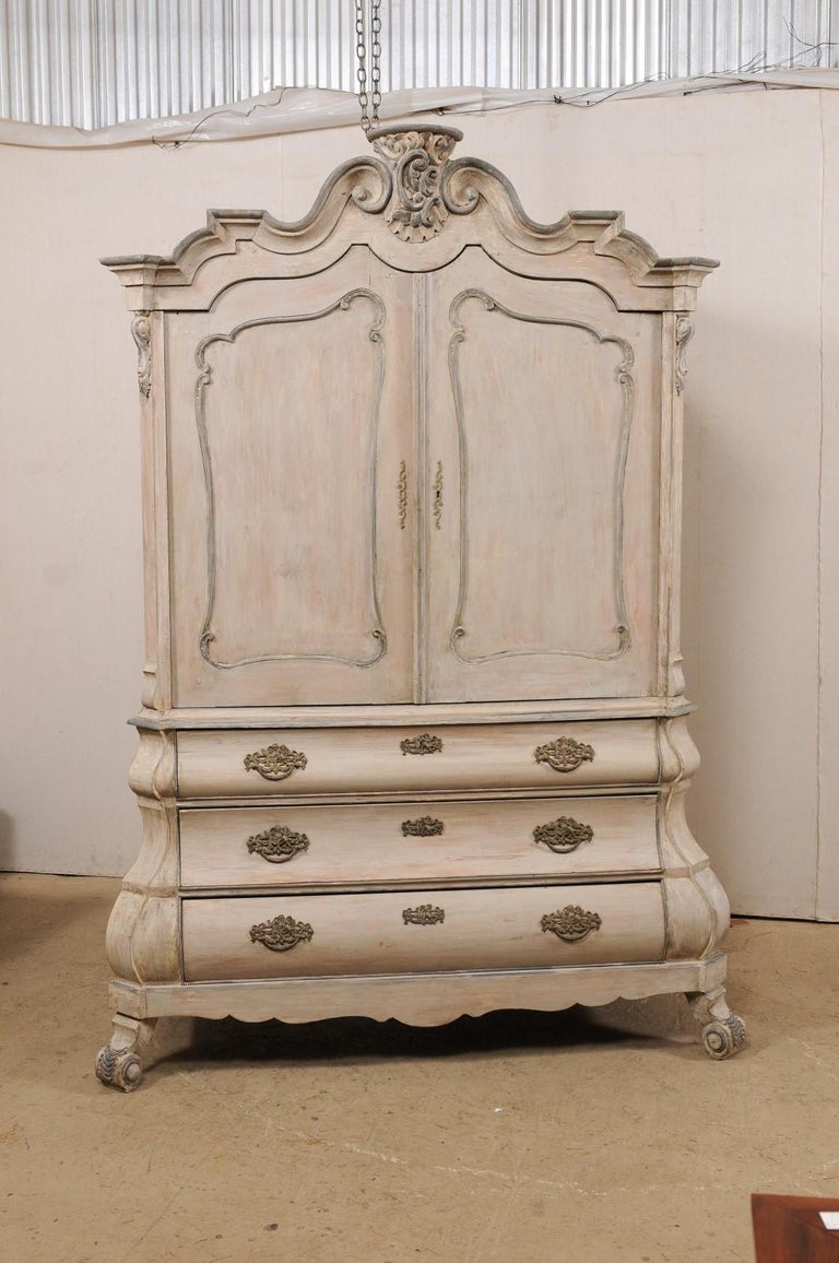 A Dutch bombé nicely carved and painted tall cabinet from the early 19th century. This antique chest from the Netherlands features a Classic Dutch style with ornately carved pediment crowning above the upper cabinet which houses a pair of