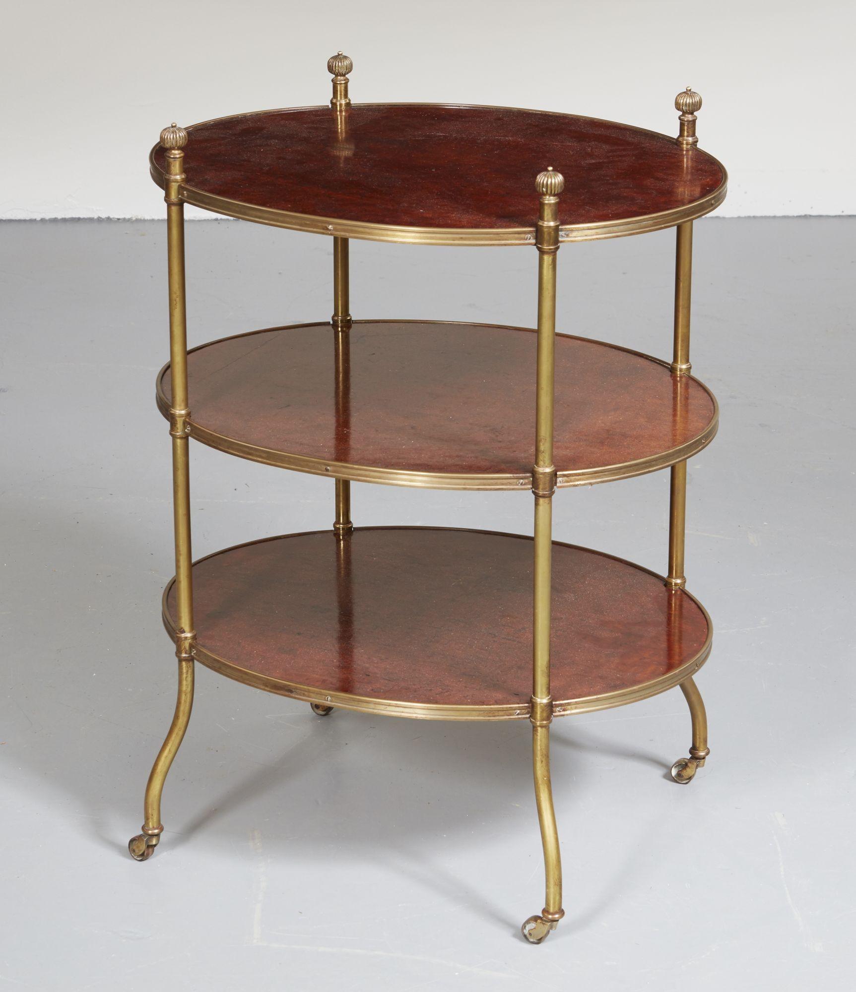 An early 19th century campaign table of oval shape with three tiers of beautiful plum pudding timber, each banded with reeded brass and connected together on four brass legs with decorative finials to the top and outturned bases ending in find brass