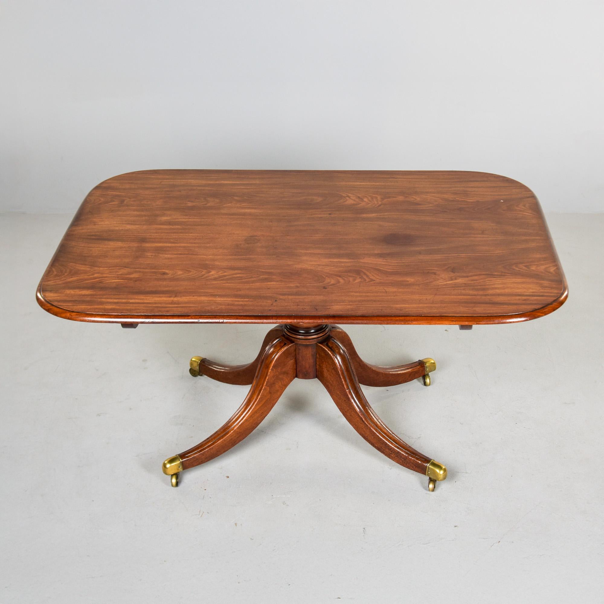 Encontrada en Inglaterra, esta mesa de caoba data de la década de 1830. La base tiene cuatro patas con casquillos y ruedas de latón originales. Tablero rectangular con esquinas redondeadas, desgaste y pátina honestos y herrajes del tablero