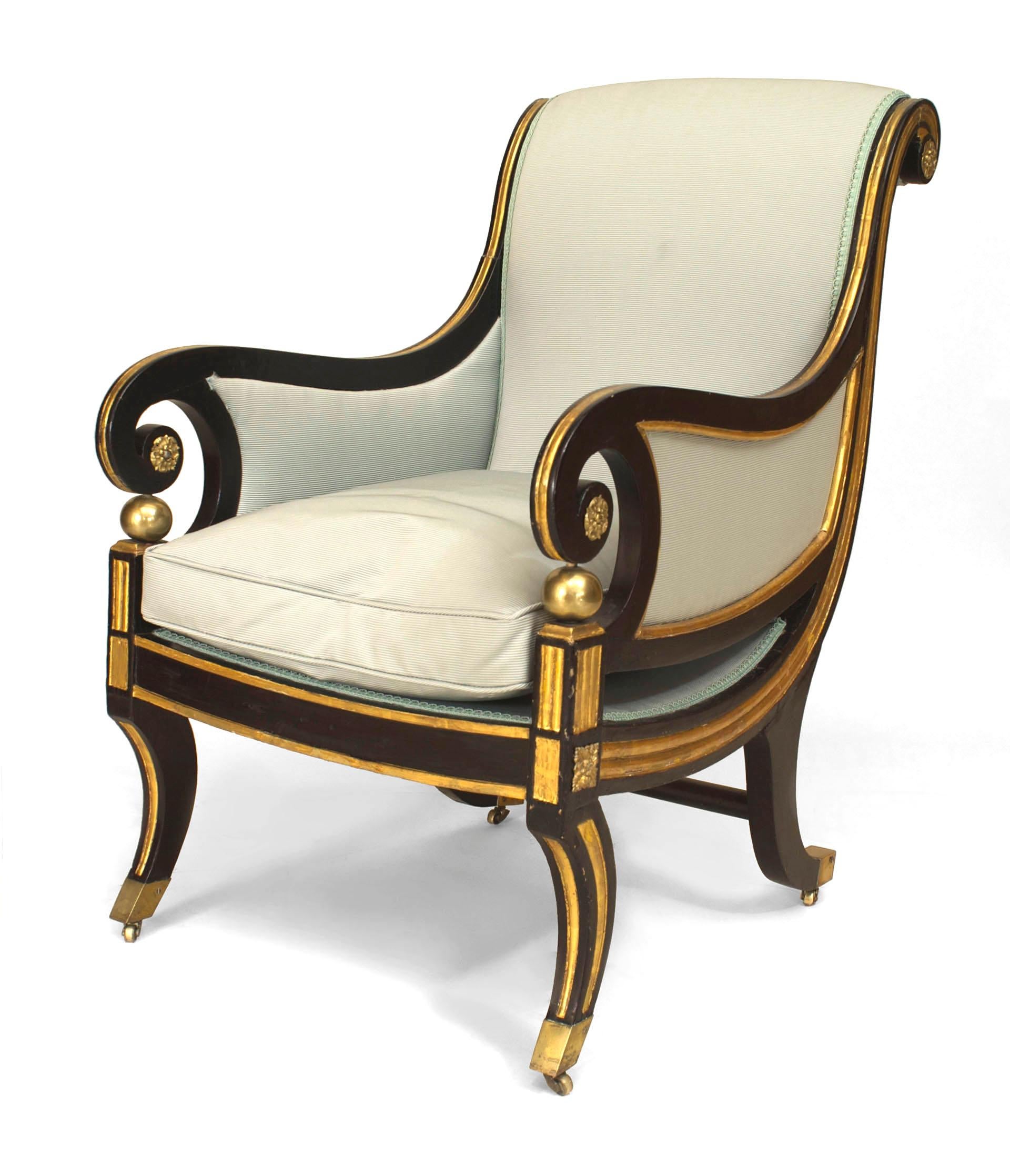 Early nineteenth century cream upholstered club chair composed of ebonized and gilt trimmed wood with a sleigh back and brass trimmed curlicue arms resting upon gilt spheres with four curved legs and an apron adorned with a brass decal.