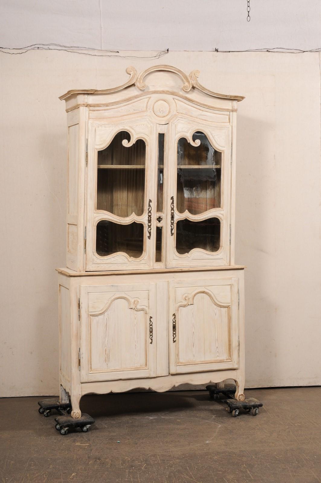 Un buffet à deux-corps in legno intagliato e dipinto in stile Luigi XV, risalente agli inizi del XIX secolo. Questa vetrina antica proveniente dalla Francia è sormontata da un frontone ad arco a voluta intagliato, che sovrasta il mobile superiore