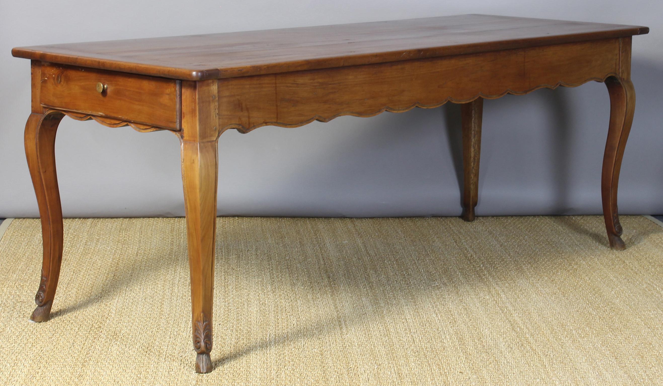 A simple and elegant early 19th century French farm or dining table in cherrywood with molded scalloped apron and cabriole legs terminating into delicately carved feet. The long and narrow table has a wonderful patina and an operating drawer at one