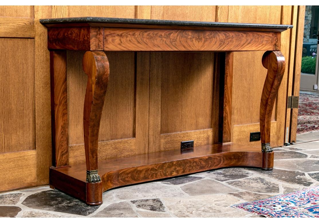 An exceptional antique French first empire marble-topped figured mahogany console table, circa 1800. The rectangular Belgian black-gray flecked marble top surmounts a conforming frieze with a long drawer, without hardware, the handholds underneath.