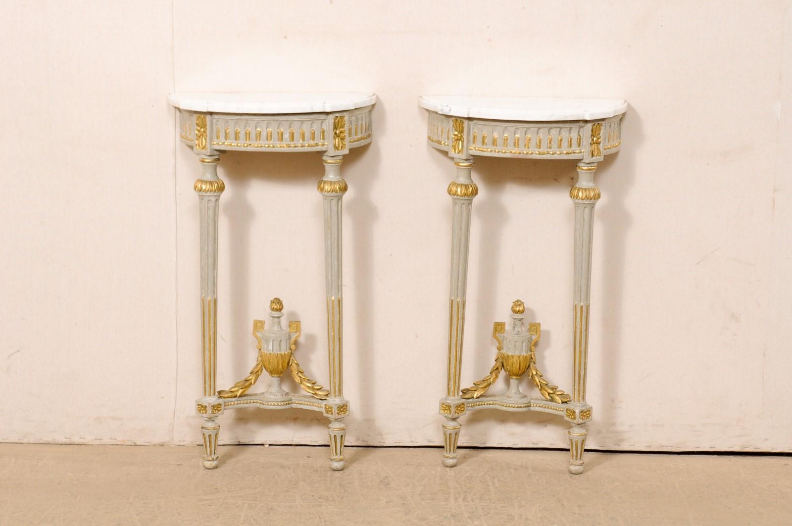 A petite pair of French Neoclassical wall consoles, with their original marble and finish, from the early 19th century. This Period Neoclassical pair of tables from France each feature a white marble, half-moon/demi shaped top, with rectangular