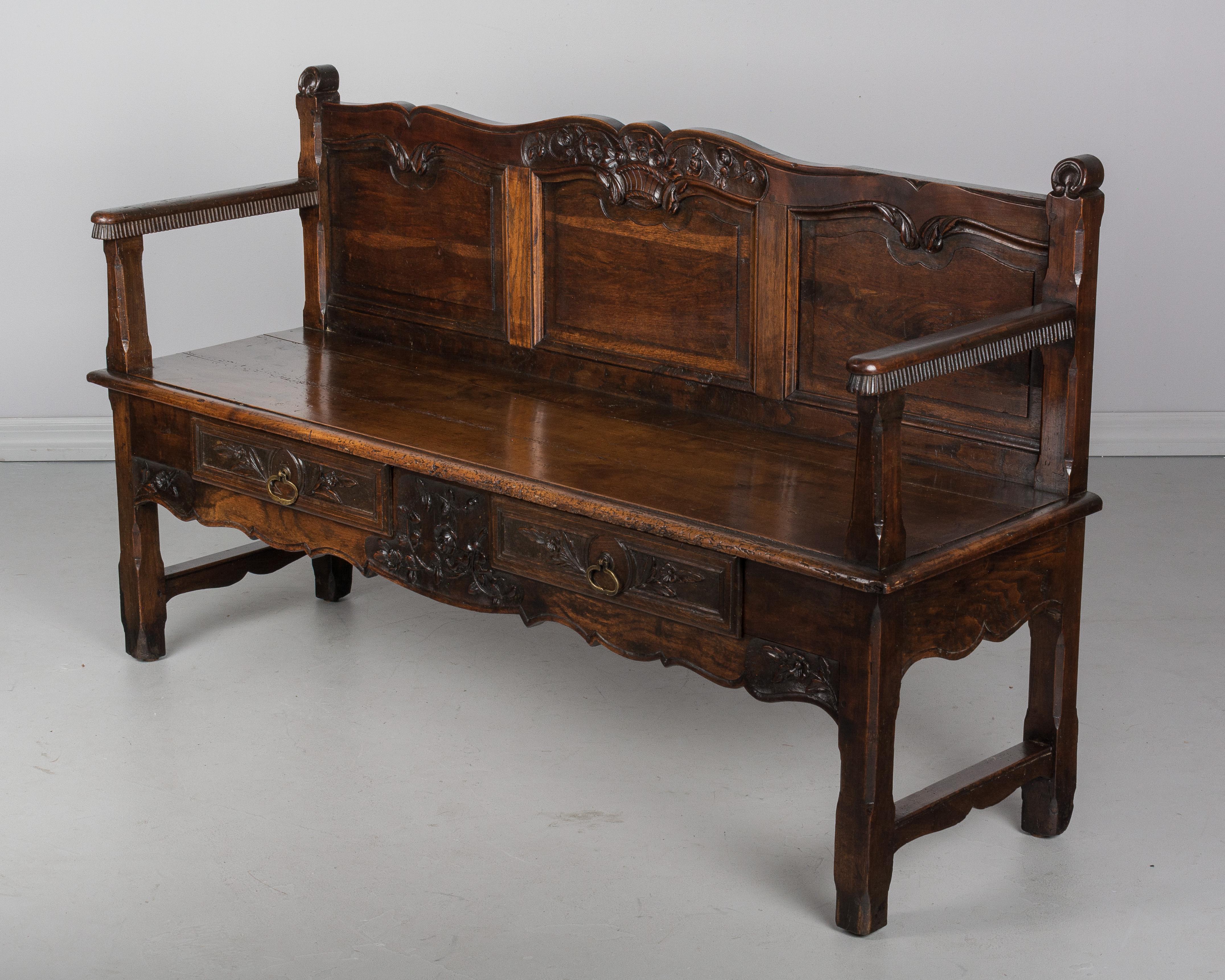 An early 19th century French Provencal bench made of oak and cherry woods with beautiful hand-carved floral decoration. Under the seat are two dovetailed drawers with brass pulls. Sturdy and well-crafted using pegged construction. Waxed patina. All