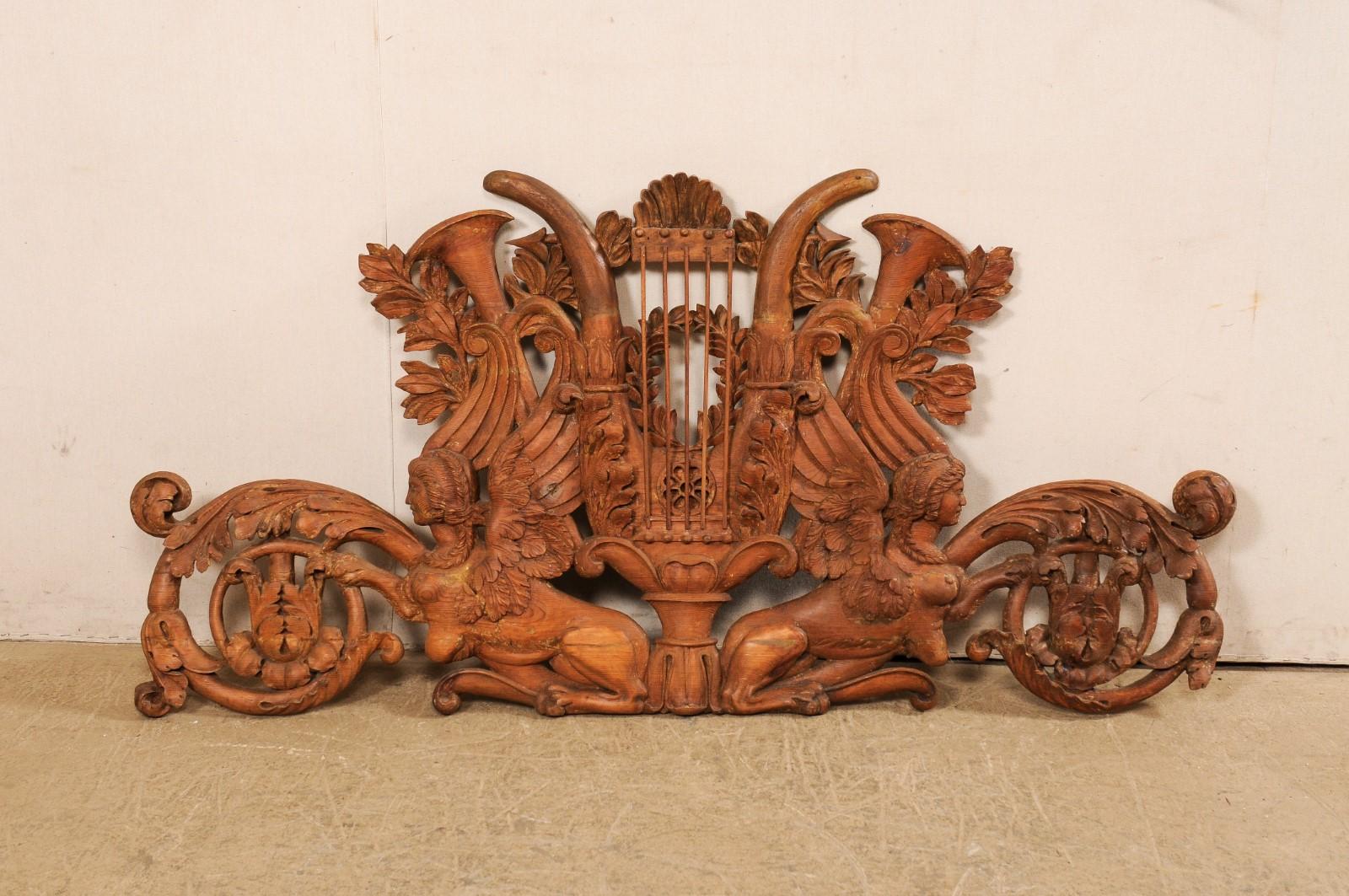 An Italian pierce-carved wood wall plaque in Sphinx motif from the early 19th century. This antique wall decoration from Italy has a beautiful pierce-carved pine wood body featuring a pair of outward-facing sphinx, flanking a wreath and shell