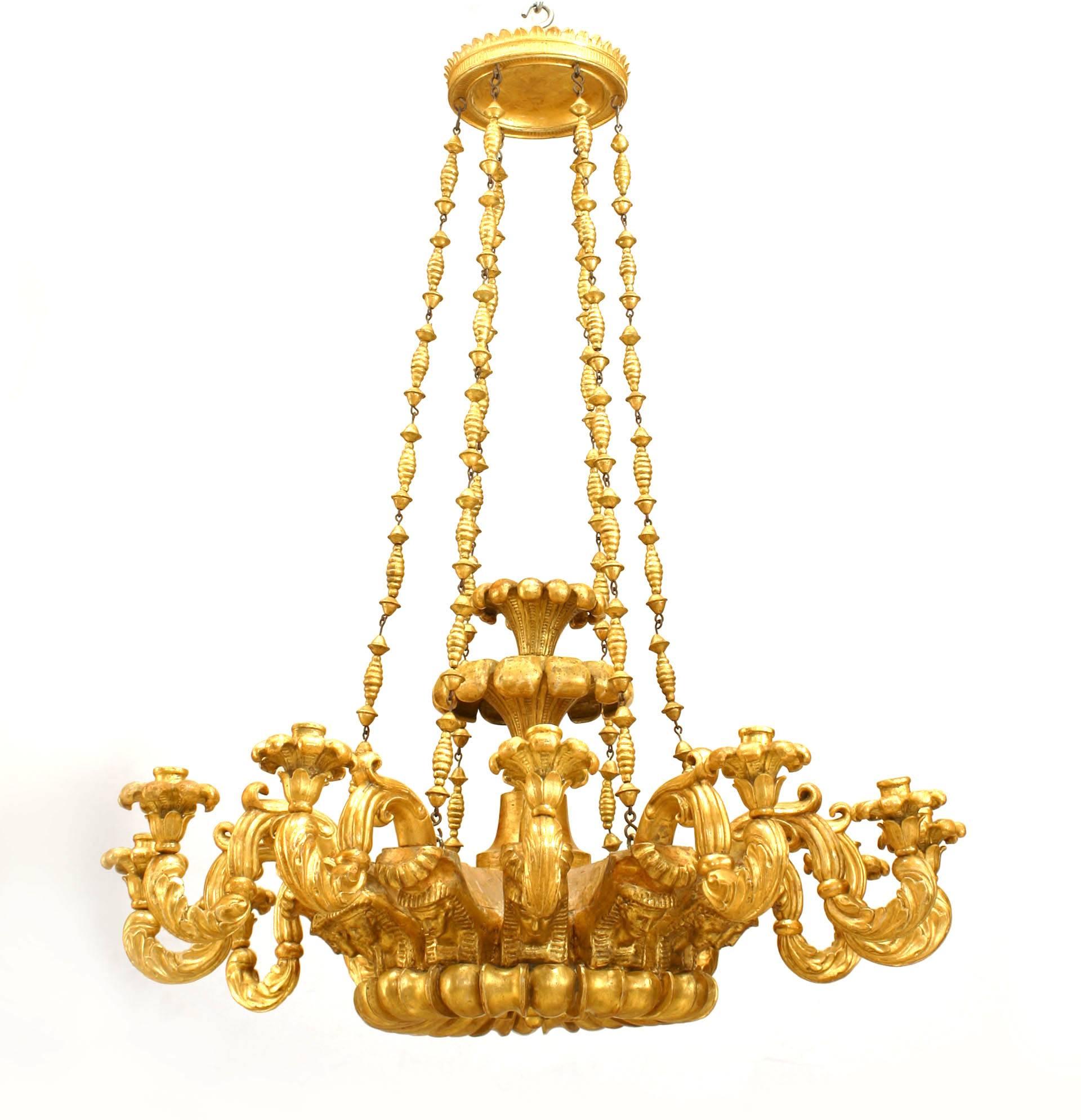 Italian Neo-classic (18/19th Century) gilt wood chandelier with 12 arms emanating from a carved fluted & floral round base with Egyptian heads & supported by 6 spool chains.

