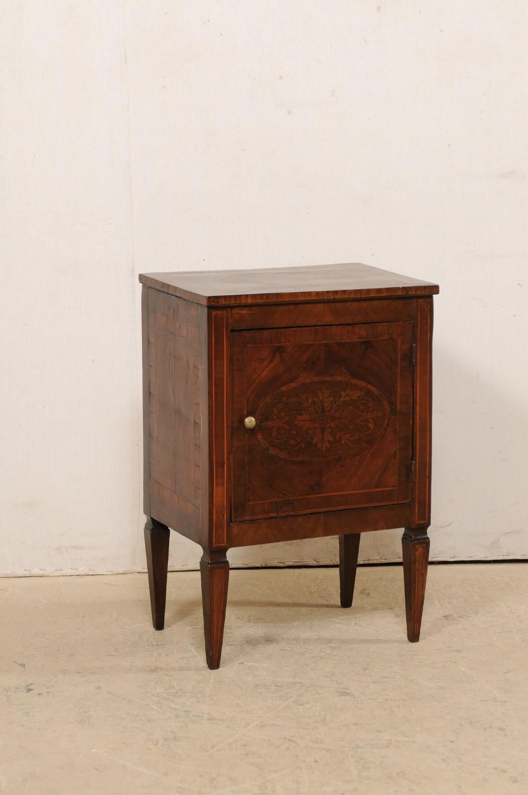 An Italian small-sized neoclassical commode with decorative foliage inlay from the early 19th century. This antique cabinet from Italy features decorative inlay throughout; with an oval-shaped foliage motif medallion at top center, and repeated at