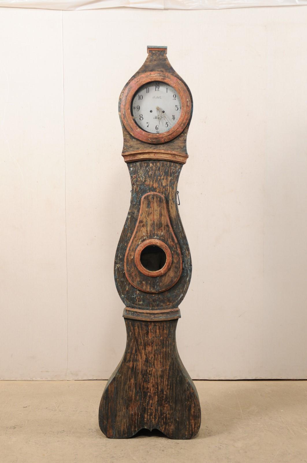 An early 19th century Northern Swedish painted wood grandfather clock. This antique floor clock from Sweden (Northern region) features a raised top crest or bonnet with flat top, with face, neck, and belly accented with trim molding, and raised on a