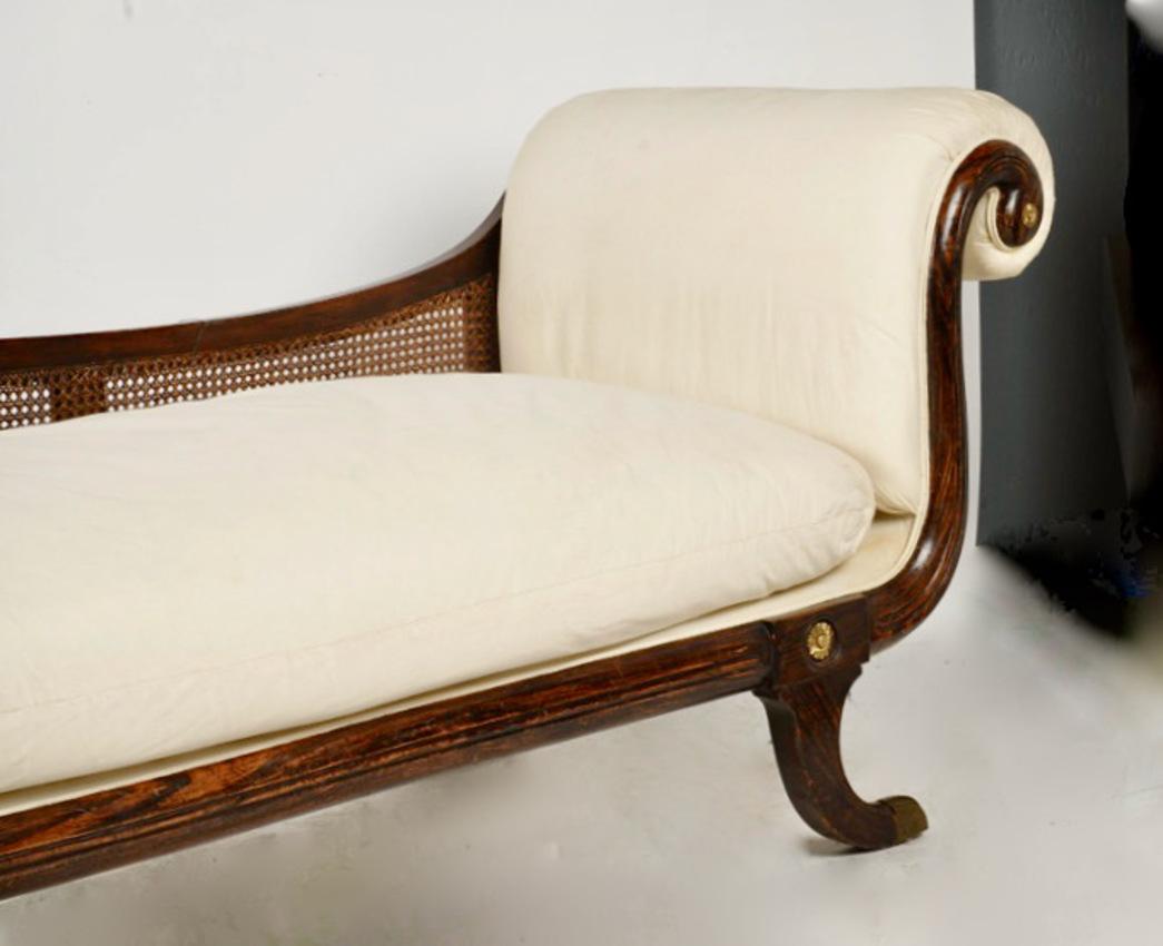 Il s'agit d'un magnifique exemple de lit de jour ou de récamier classique de style Régence. Le lit de jour est doté d'un cadre en faux bois de rose et d'un dossier en rotin. Les extrémités sont ornées de rosettes en bronze doré. Il a été