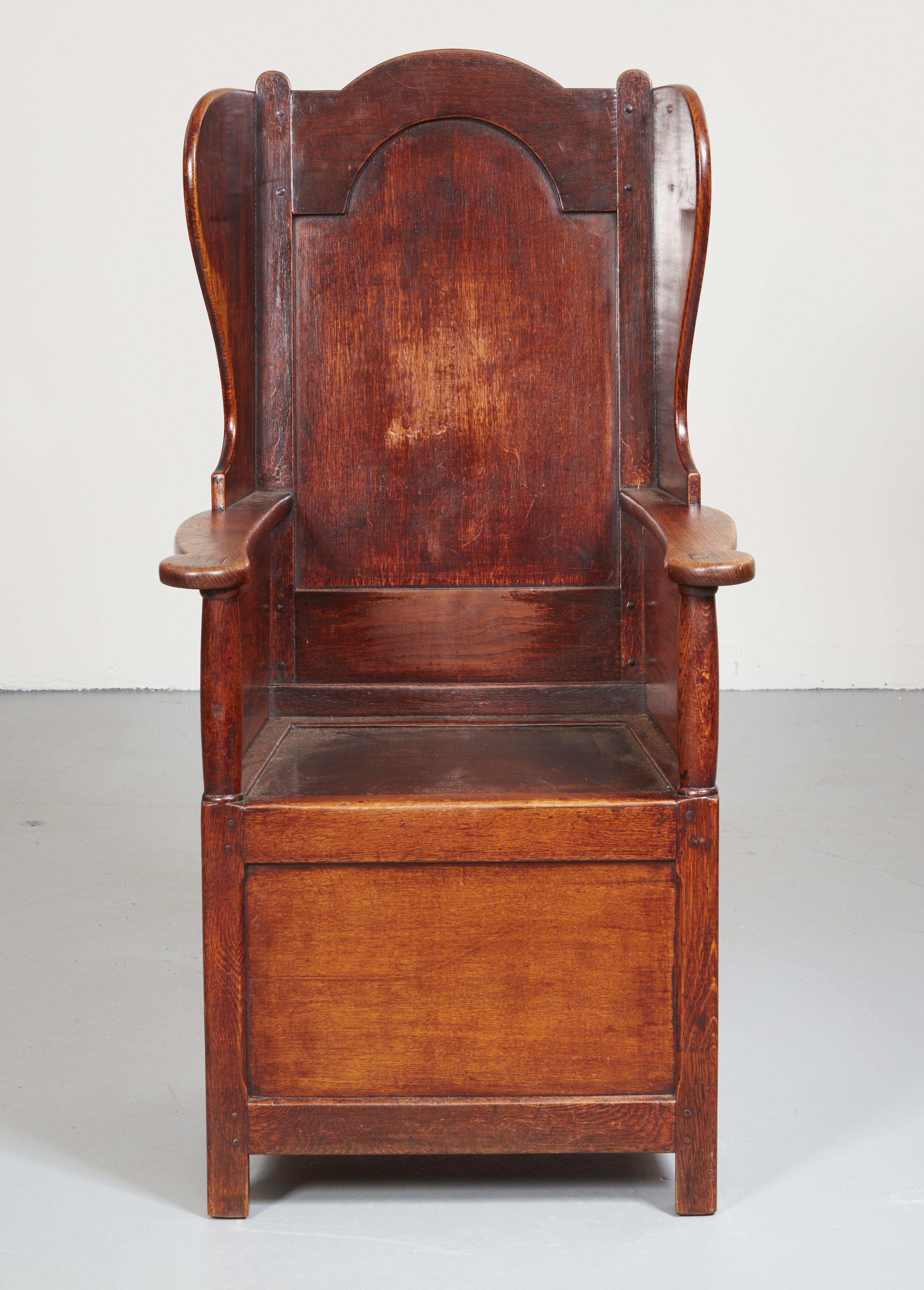 An early 19th century oak Welsh lambing chair with very good color. Paneled back and sides, shaped top and curved wings on flattened arms with rounded handles on box base standing on stile legs. A distinguished chair that would make an attractive