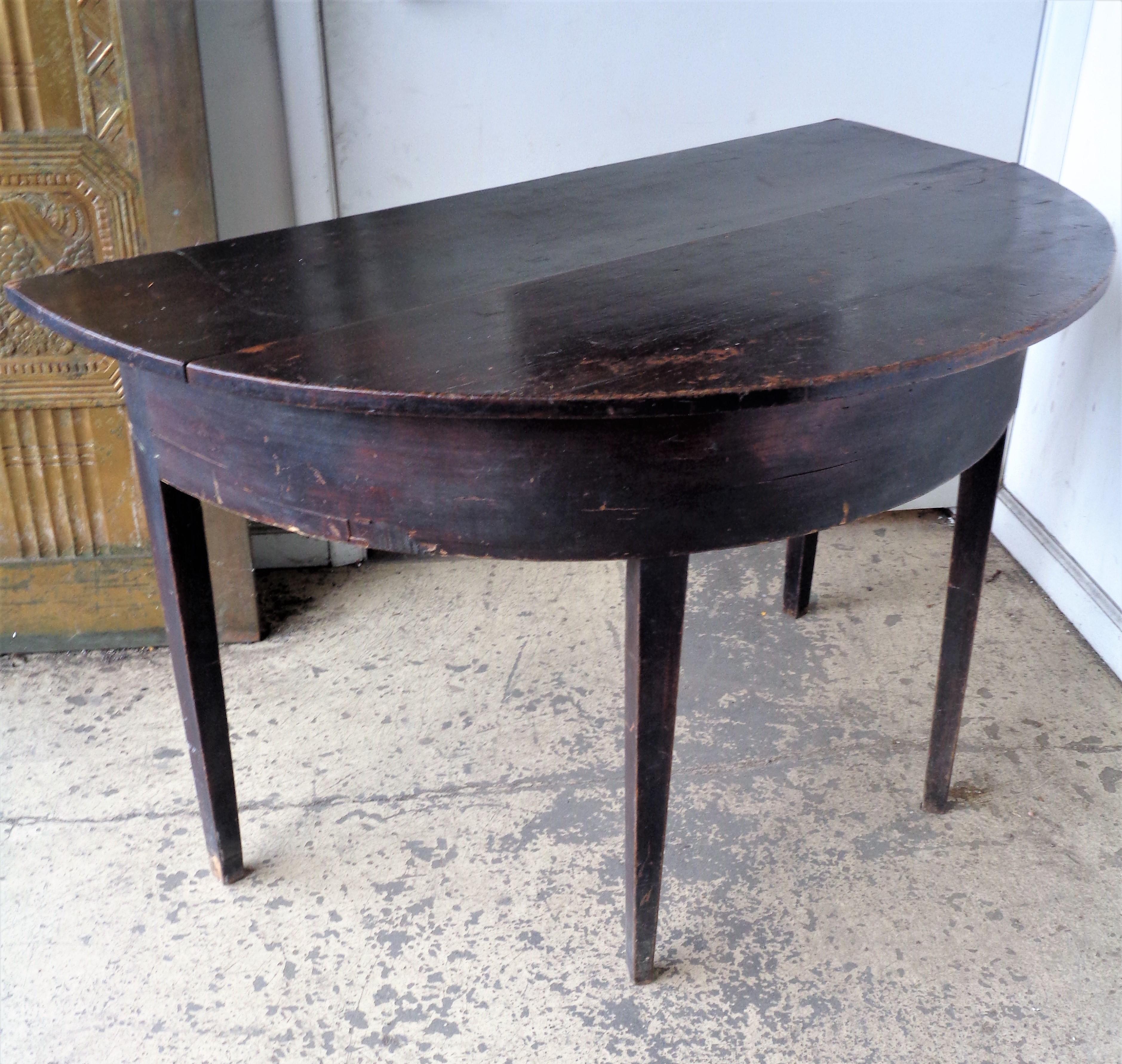 American country demilune table in overall nicely aged original old surface color. Two board over hanging wood top / half round front apron w/ original veneer / tapered legs. Circa 1830 - 1850. Good looking early antique table. Look at all pictures