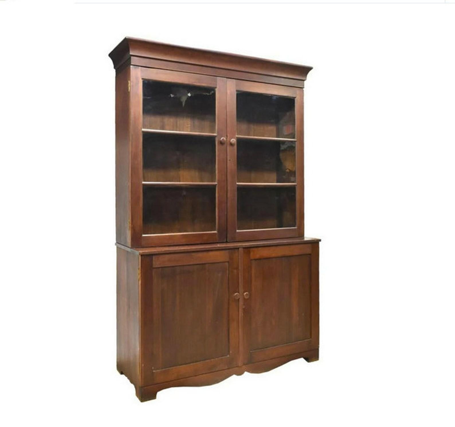 An imposing antique two-piece 'mahoganized' cherrywood American stepback cabinet from the early 19th century, circa 1820. Having molded cornice over glazed double doors, opening to interior shelves, lower case fitted with paneled double doors,