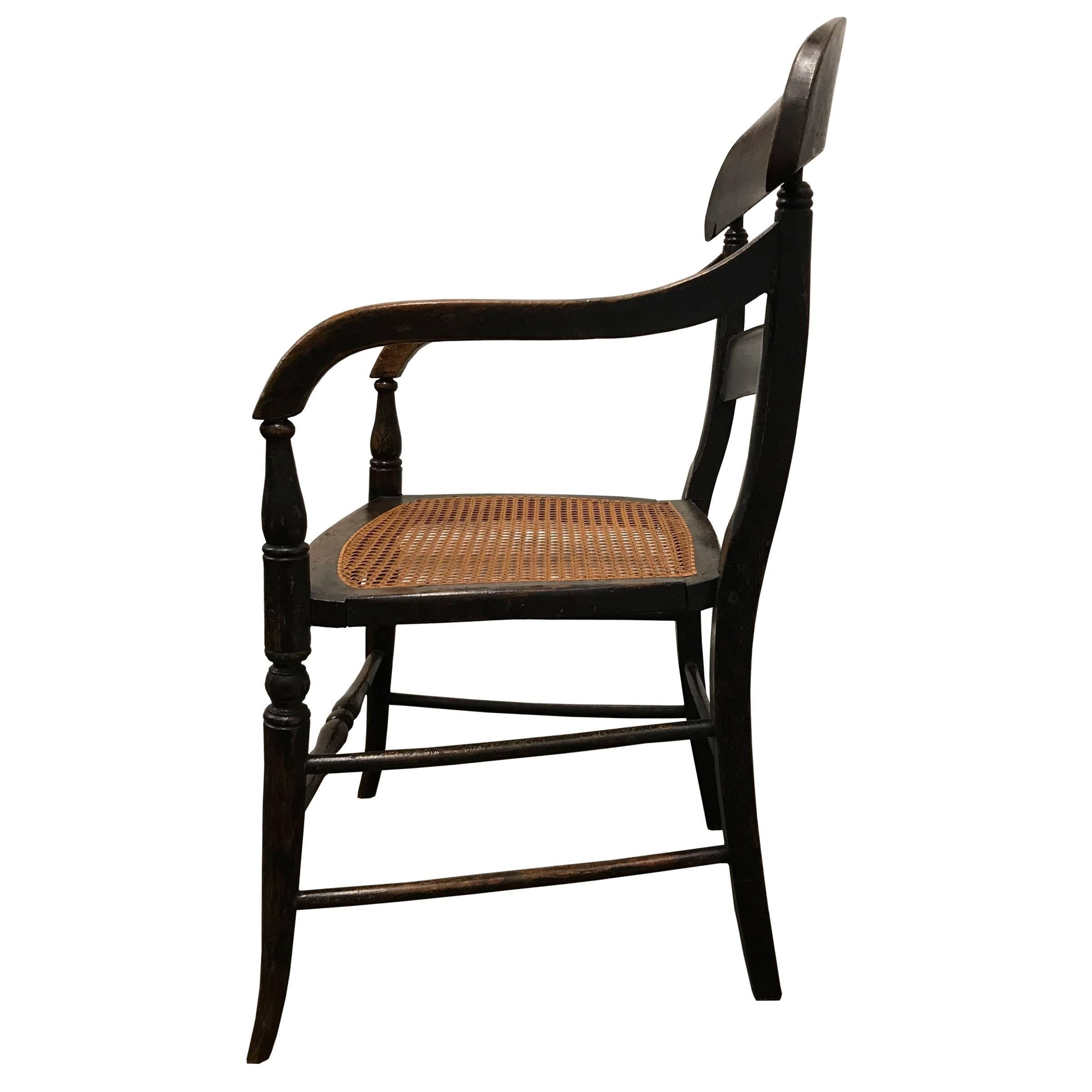 An early 19th century American Empire oak armchair with turned legs, woven cane seat, and a well worn front spindle. The wood grain is faux painted, a very popular decorative painting technique in the early 19th century in America.