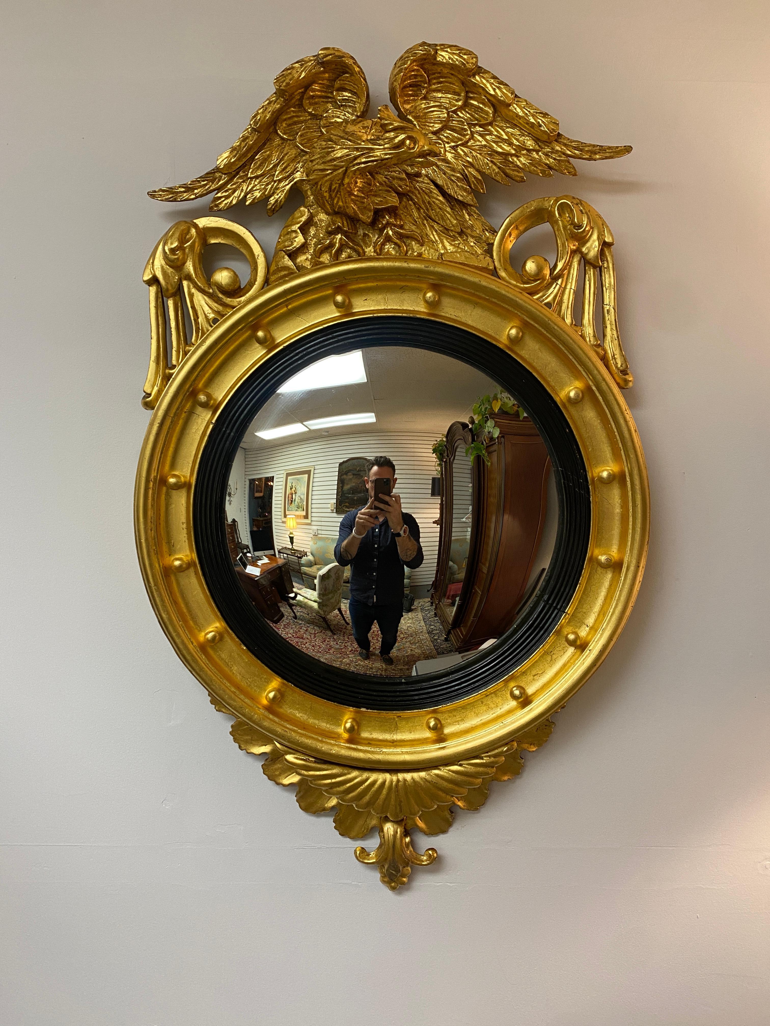 This is a handsome and completely restored American Federal convex bullseye gilt mirror. Features a wood carved perched eagle over flanking acanthus foliage, interior circular spheres, ebonized reeded ring, and terminating at bottom with acanthus