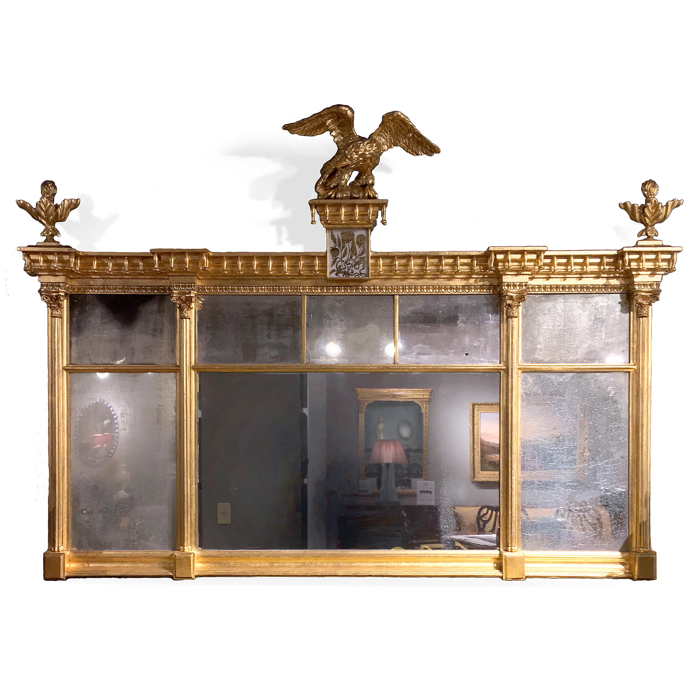 This American Federal-period overmantel composition mirror features a gilt carved wood and gesso frame. A sculpted eagle is perched above an églomisé panel depicting flowers. Separating the panels of original mirror glass are engaged Corinthian