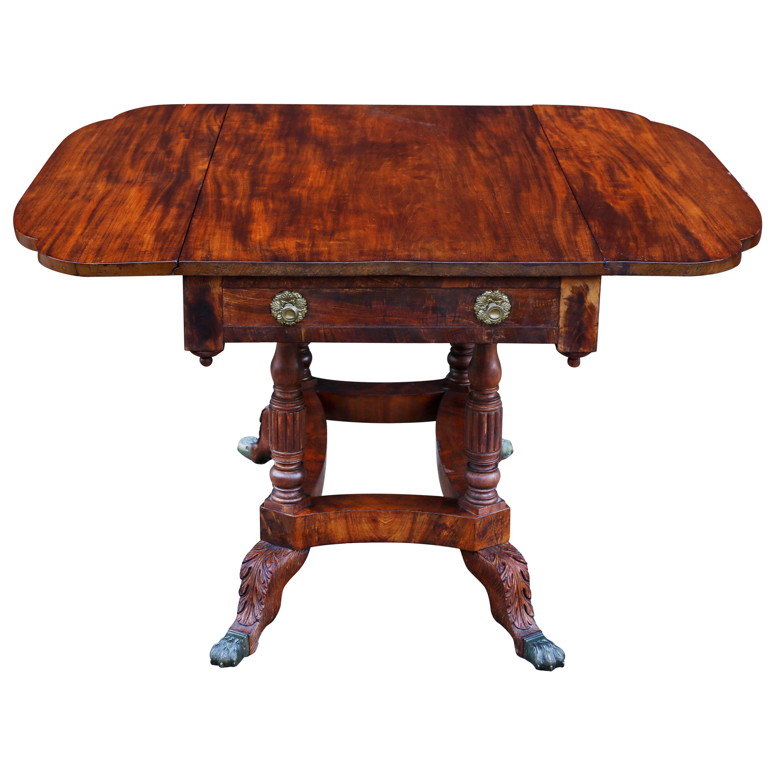 A fine New York breakfast table composed of fiddle back mahogany and exhibiting masterful carving. The Pembroke table has one drawer with original brass ormolu pulls and a matching false drawer opposite. The scalloped edged top is supported by four