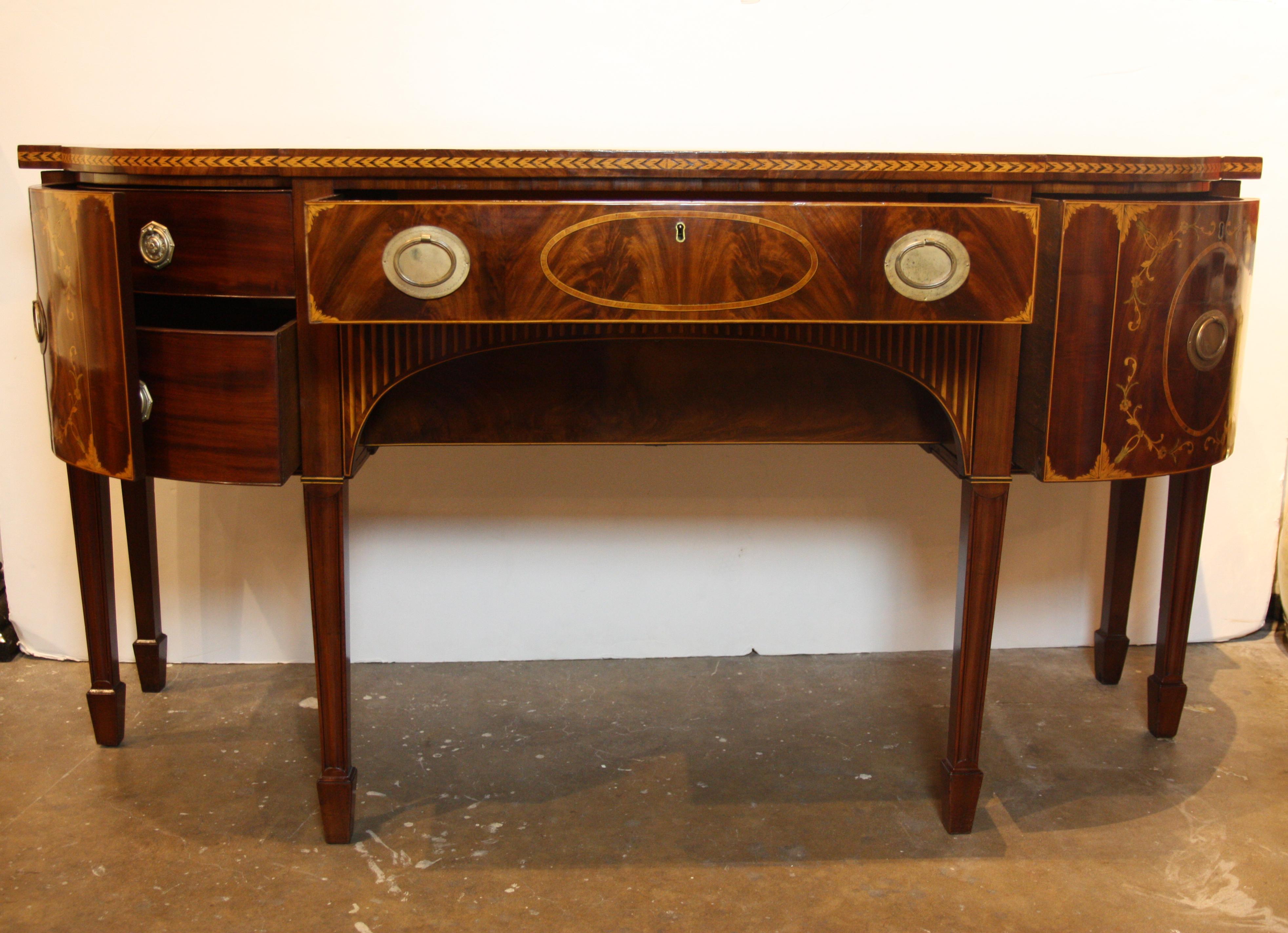 Early 19th century American Hepplewhite style sideboard in matched mahogany veneers and exotic wood inlays. Has a breakfront in the modified D-shape, a single drawer at center flanked at each side by curving doors. The right door conceals a wine