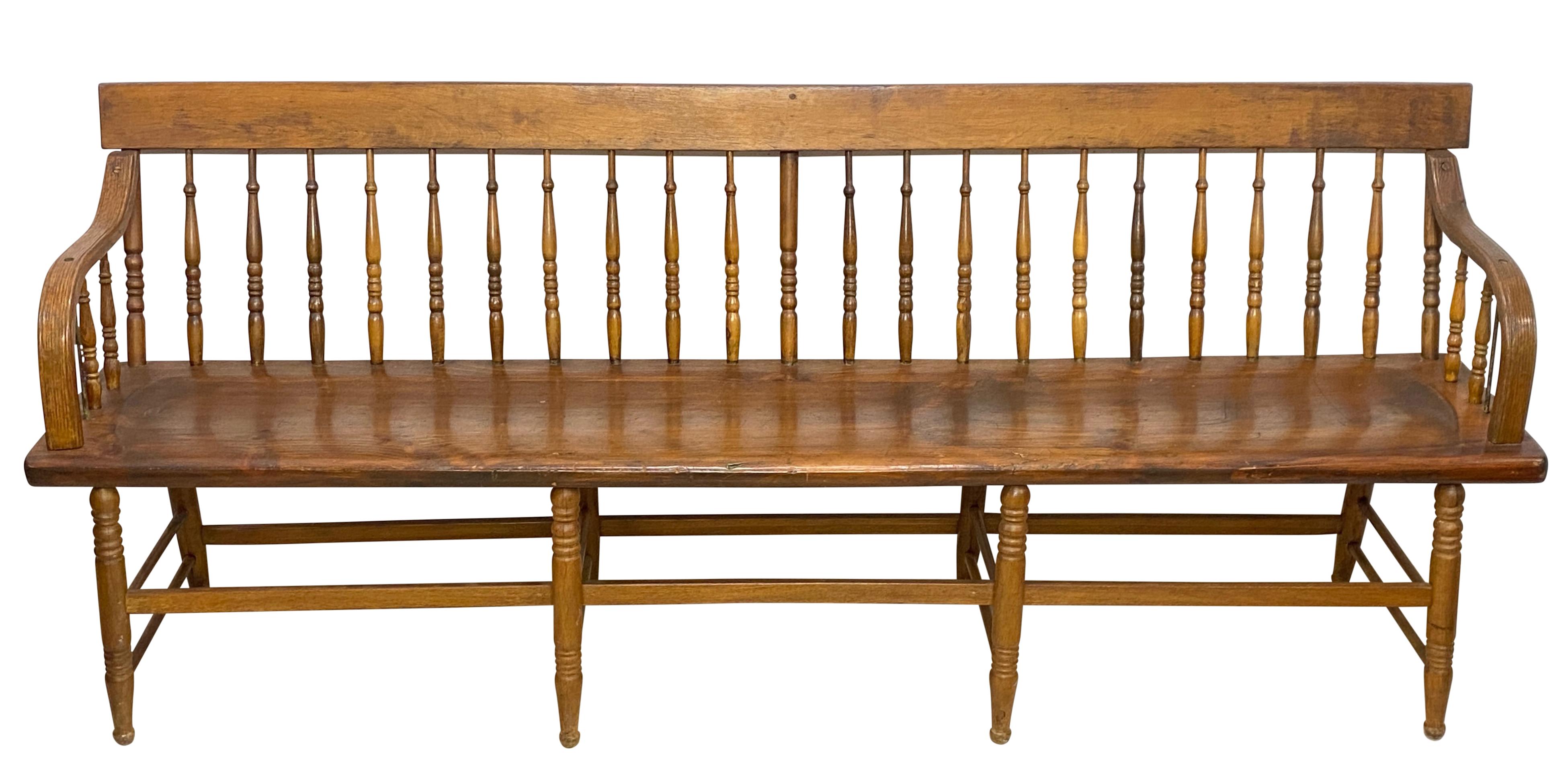 An unusually long Windsor style spindle back Deacon's Bench or farm style bench. Pine with plank seat and oak arms. Originally painted green, this bench was stripped and refinished sometime in the second half the 20th century. 
Solid and sturdy,