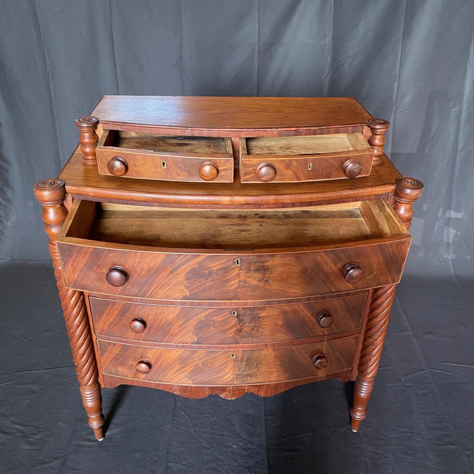  19th Century Sheraton Flame Mahogany Bow Front Chest having turret cookie cutter corners, flanked by fluted barley twist columns and onn turned legs.  There are two smaller setback drawers over four larger bowfront drawers on the chest, all fitted