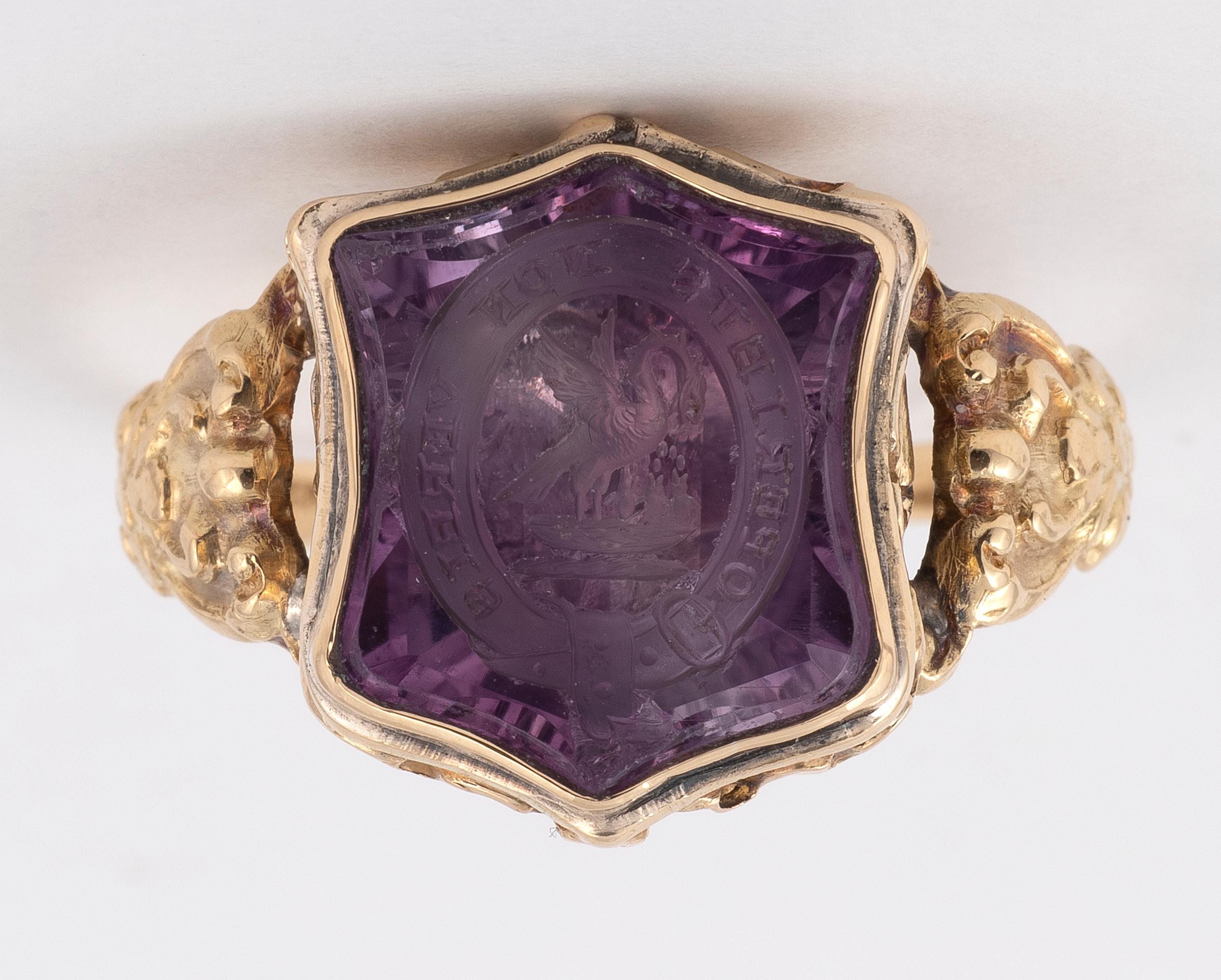 the shield shaped amethyst panel carved with the pelican plucking its breast to feed its young with the motto Operibus Non Verbis, in a domed closed back foliate setting, 
Size : 7
Weight : 4.8g
A partial inscription which translates to 'and no