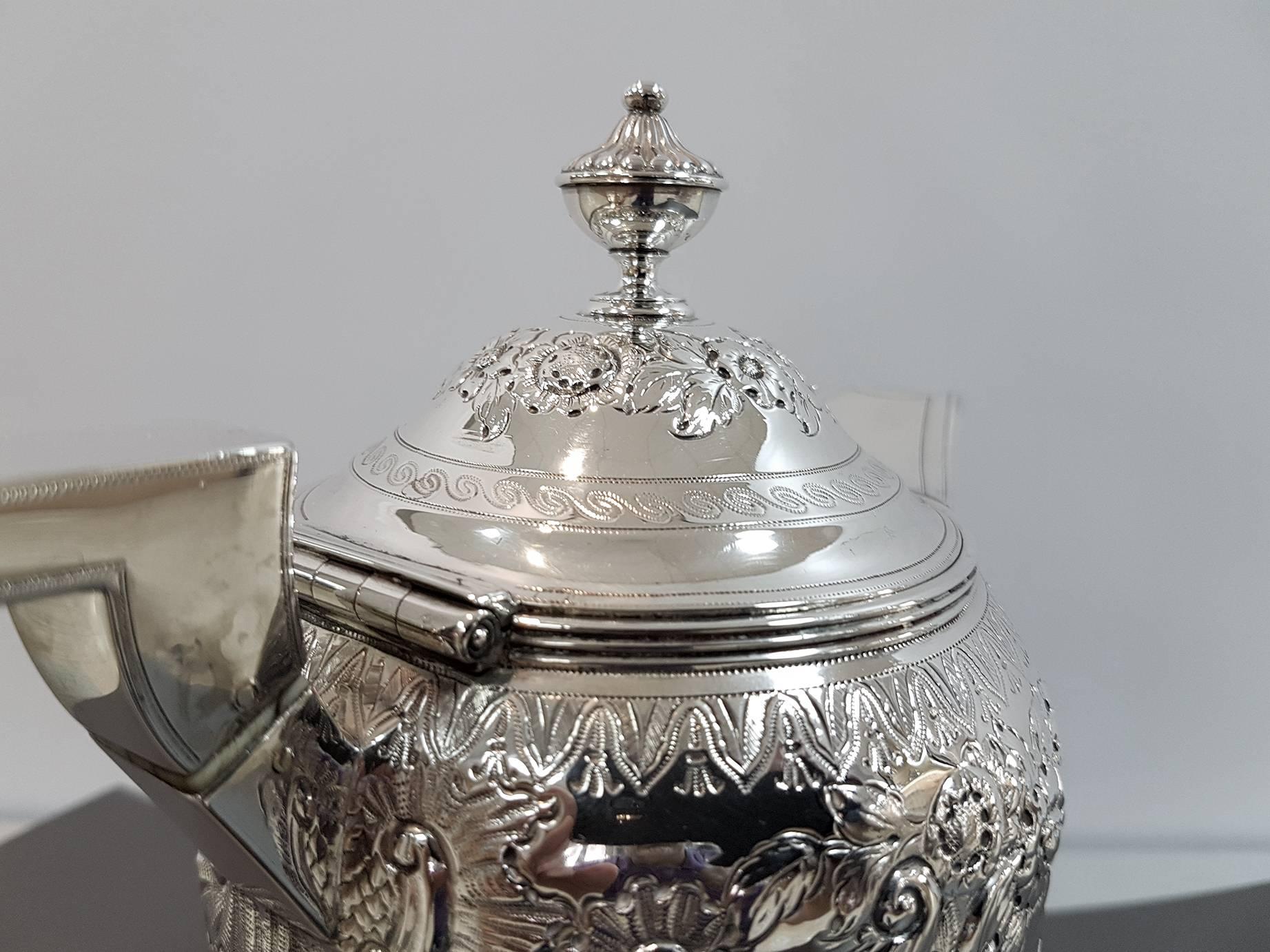 The sterling silver hot water jug has a cylindrical shape embossed and chiseled with scrolls, flowers and leaves.
The hinged lid is ceased with flowers.

Rebecca Emes & Edward Barnard
London, 1809.

790 grams.
 