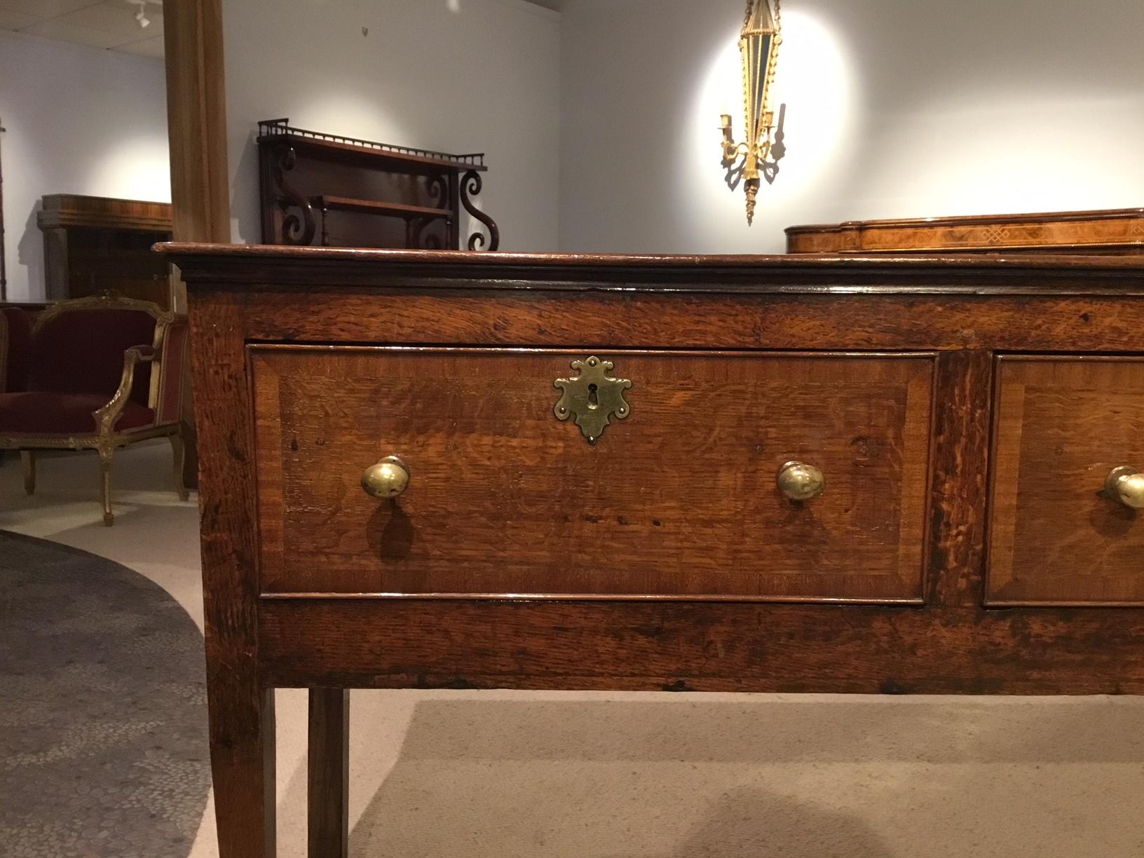 An early 19th century antique oak dresser base. Having a rectangular two plank oak top above three oak frieze drawers with brass knobs and escutcheons. Supported on square tapering supports with spade feet, English, circa 1800-1820.

Dimensions:
