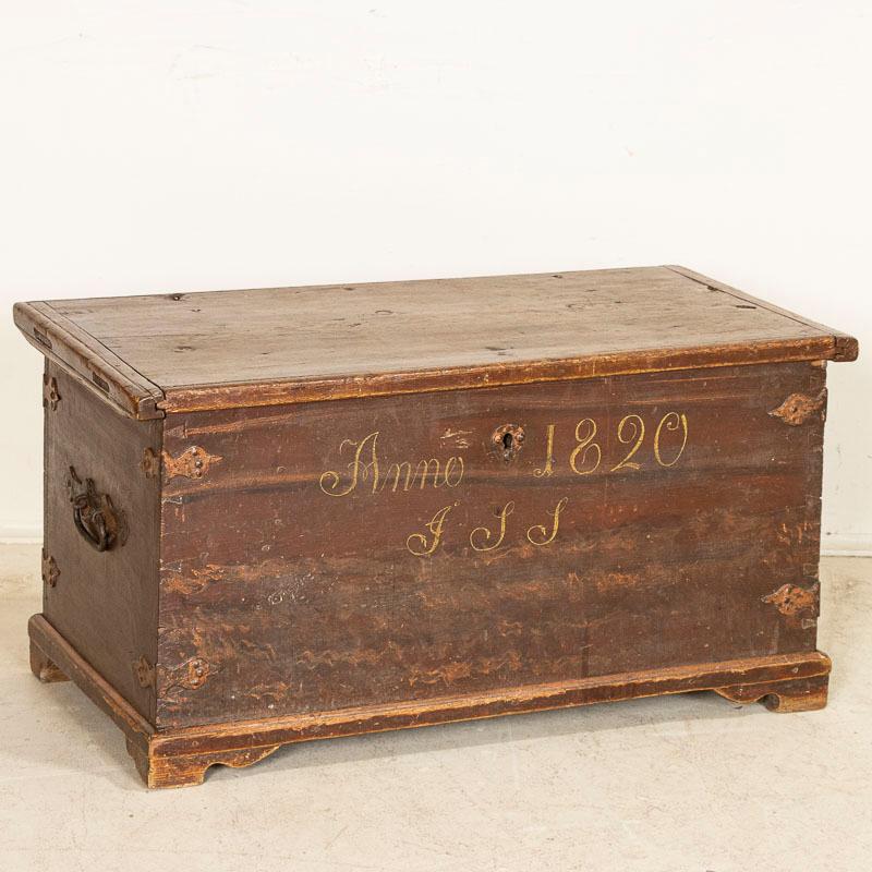 The original brick red paint has been gently distressed over generations of use, deepening the patina of this delightful flat top trunk. The hand-painted date of 1820 and lower monogram indicate it may have been part of a dowry or wedding present.