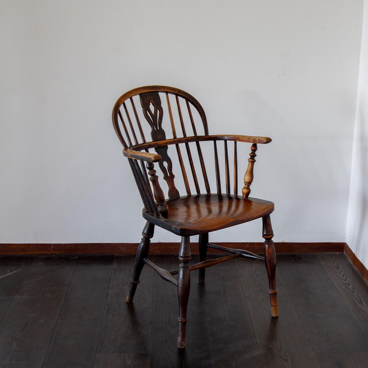 An early 19th century ash and elm low back Windsor armchair with a fruitwood splat above a solid saddle shaped seat, on turned legs connected by an 'H' stretcher.